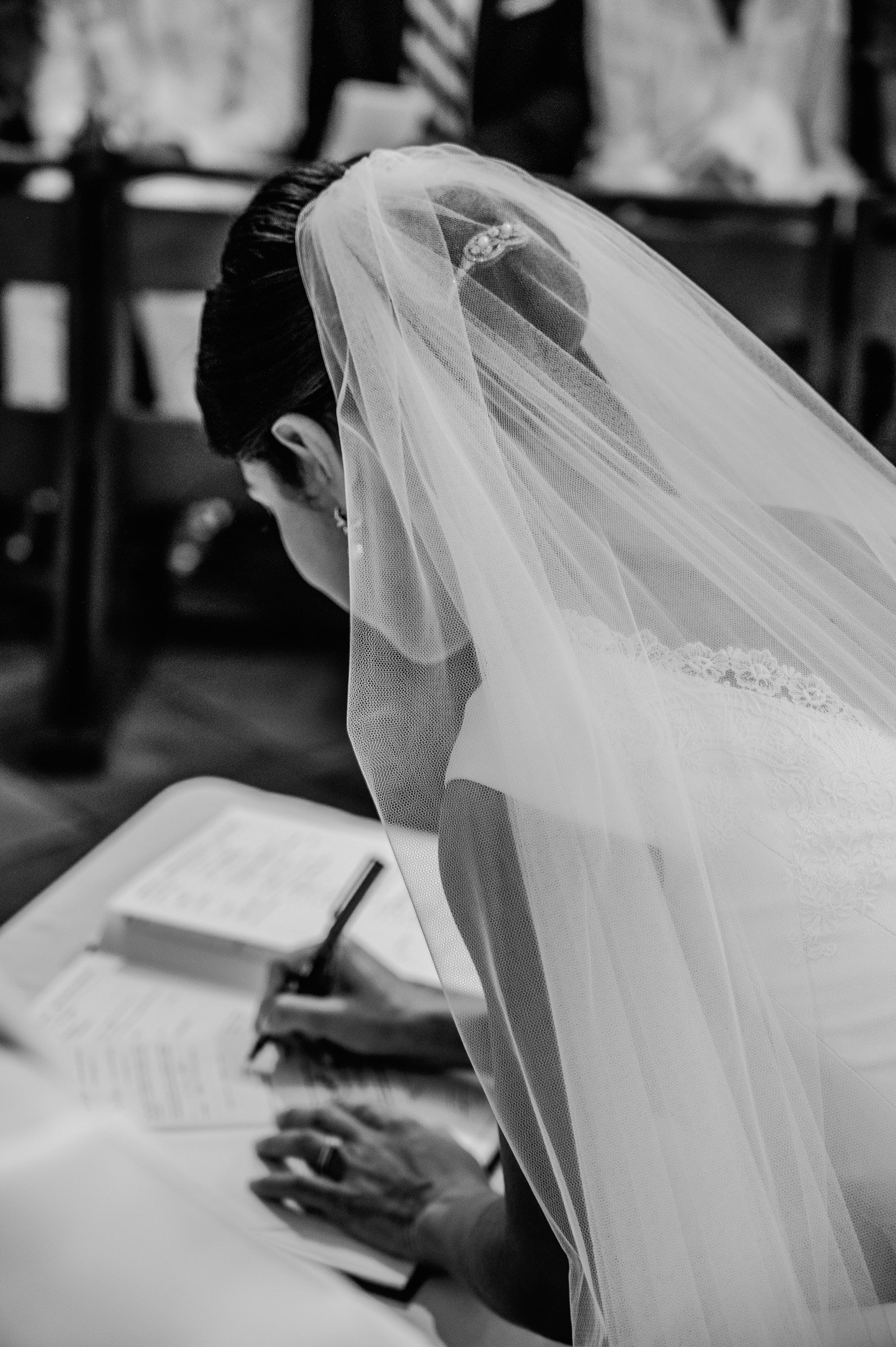 Une femme portant un voile de mariée lit un livre, assise à une table, en arrière-plan flou.
