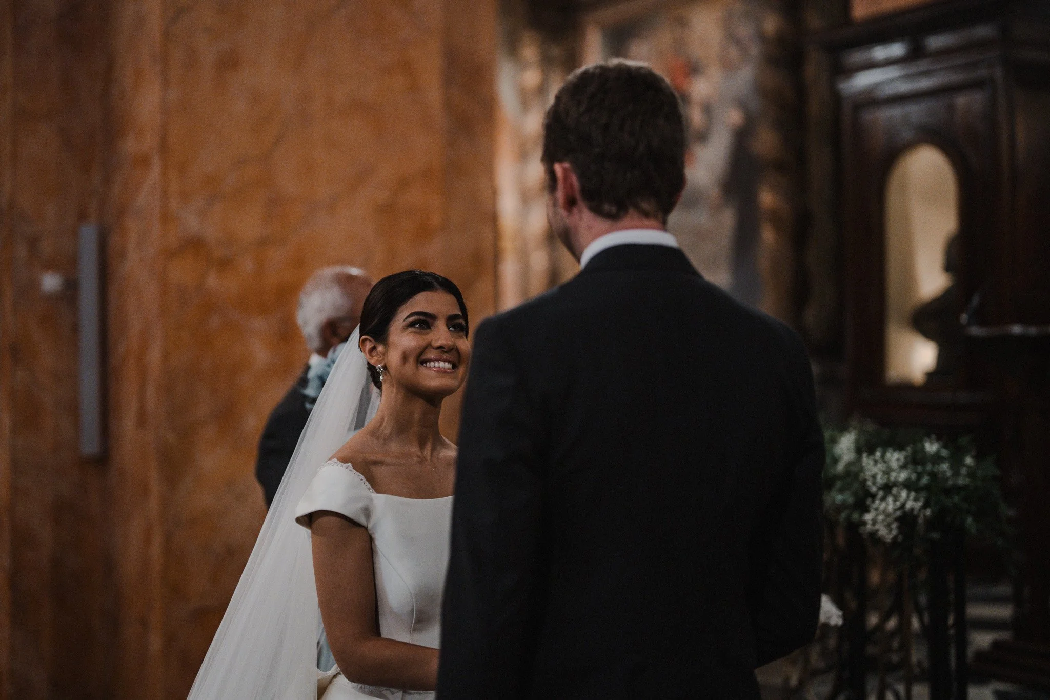 Un couple de mariage échangeant leurs vœux dans une salle décorée de manière élégante, avec la mariée souriant et regardant son partenaire.