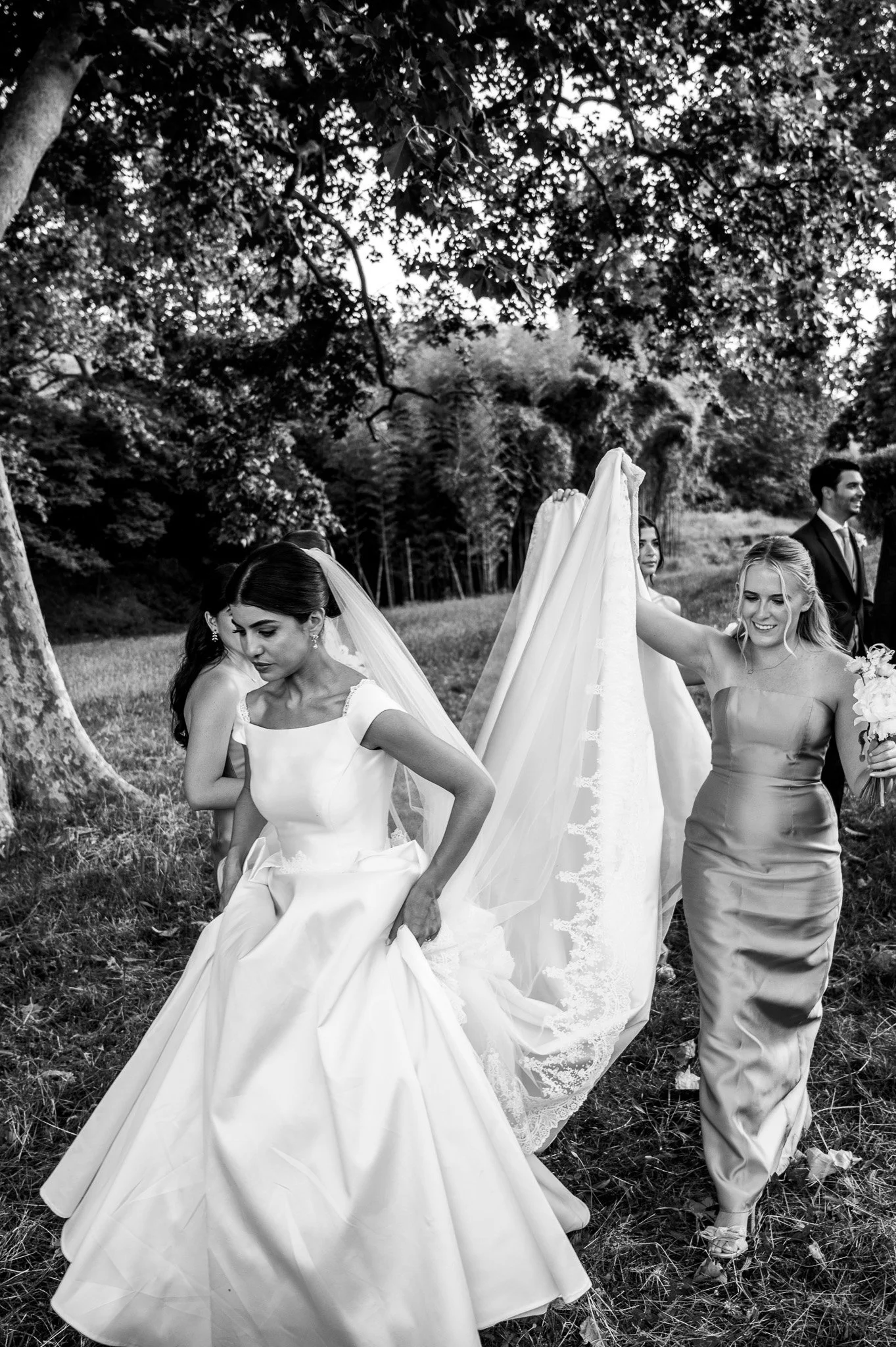 Groupe de personnes lors d'une mariée en plein air entre les arbres, en vêtements de mariage, en noir et blanc.