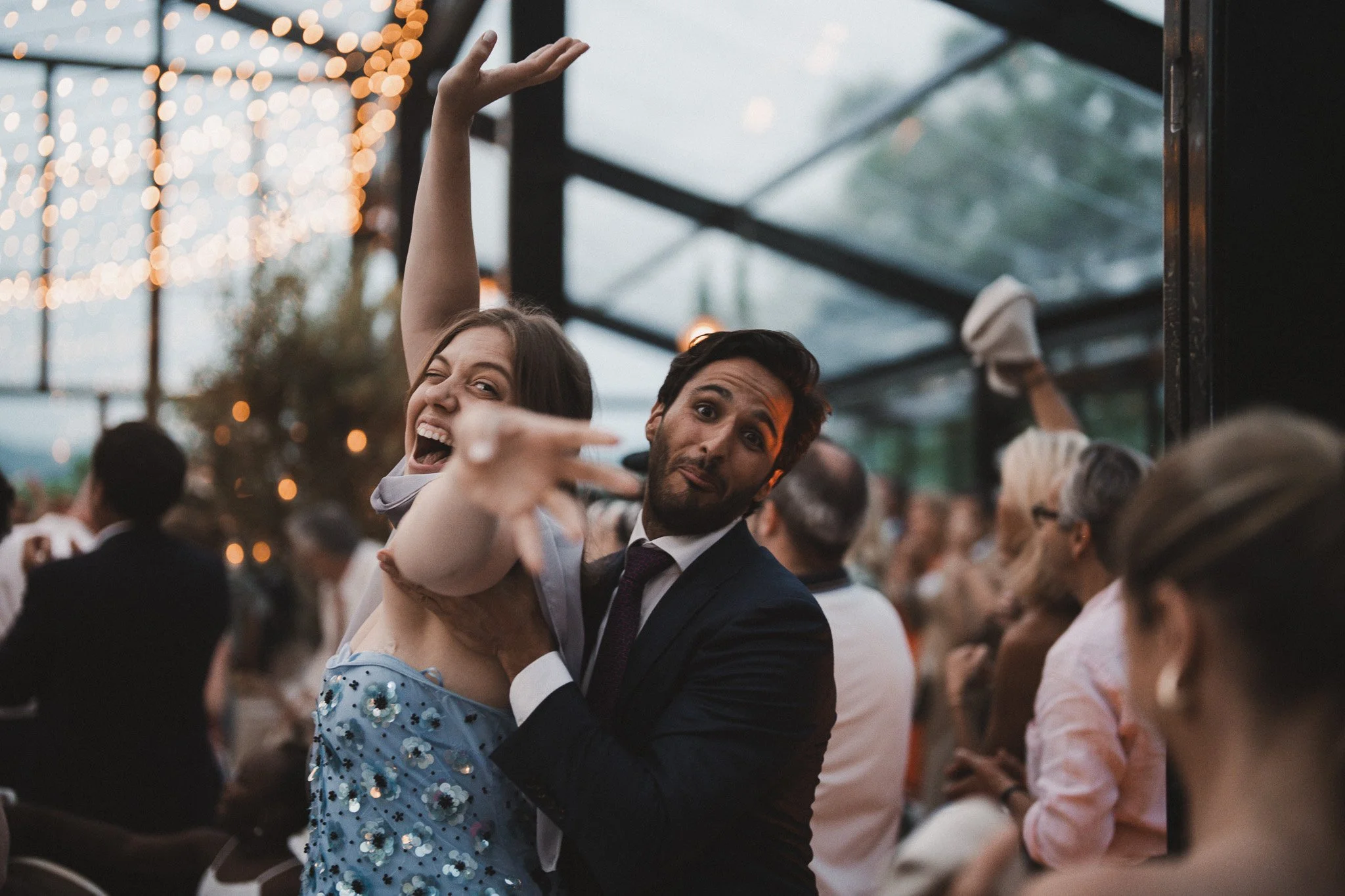 Deux personnes dansant ensemble lors d'un événement, une femme souriante avec une robe à sequins bleus et un homme en costume, sous une structure de verre avec des lumières décoratives