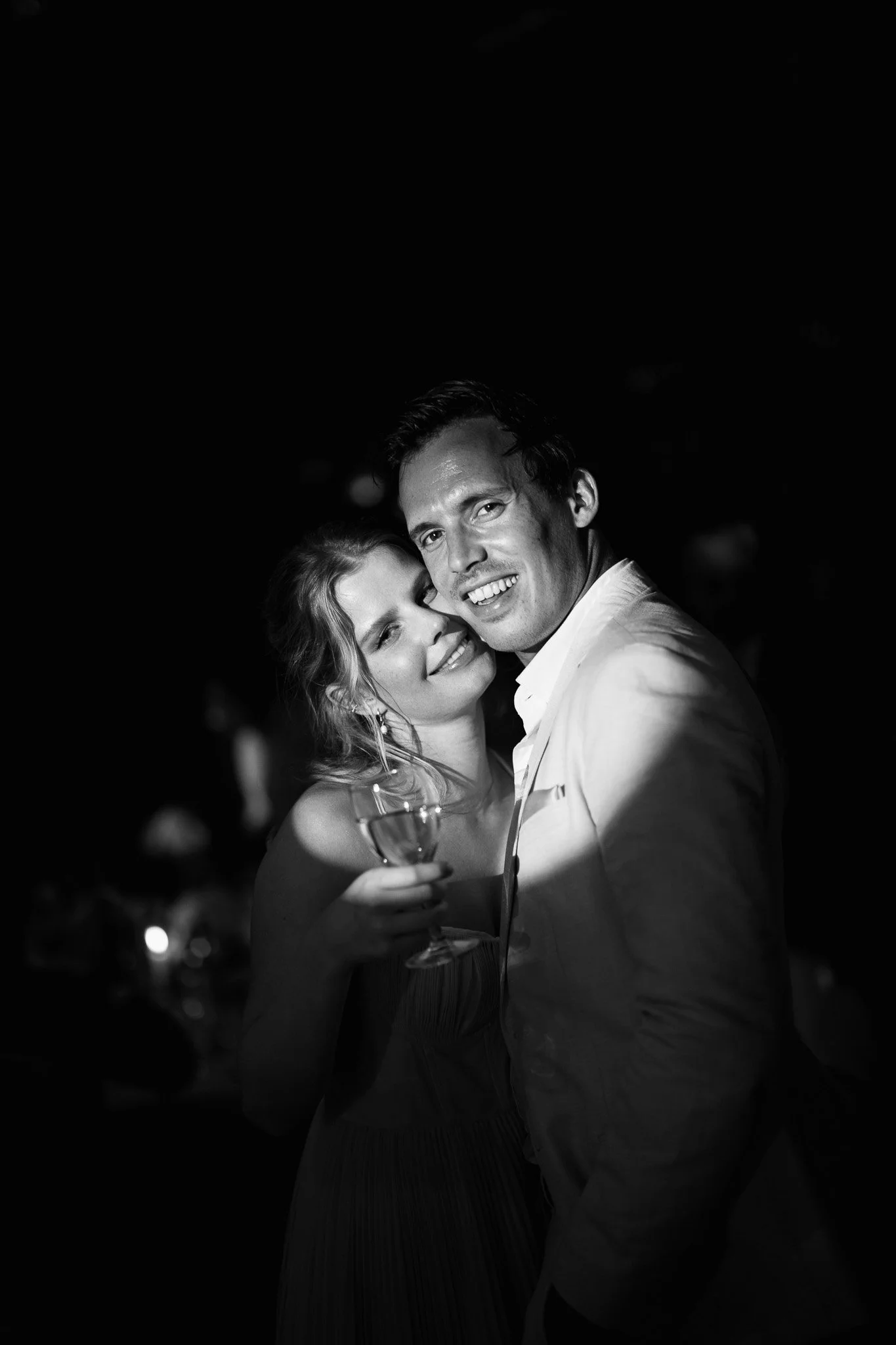 Un couple en train de danser lors d'une soirée, avec la femme tenant un verre de vin, en noir et blanc.
