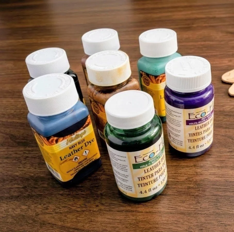 Six bottles of leather dye in various colors on a wooden surface.