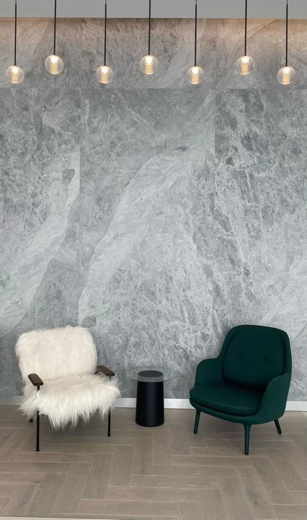 Modern seating area with sculptural gray marble wall, pendant lights, white fur lounge chair, green armchair, and black side table