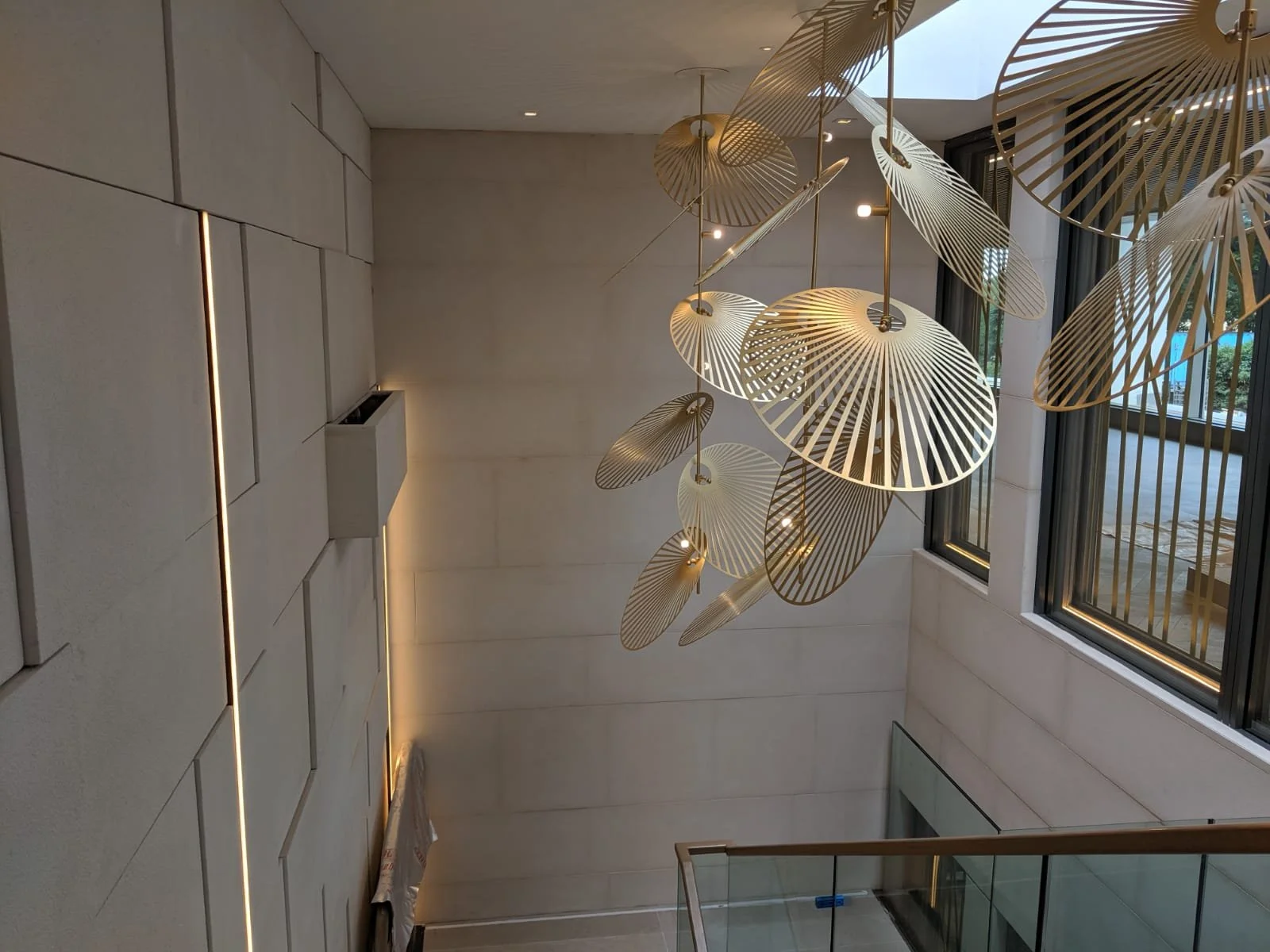 Modern lobby staircase with a large cluster of gold and white geometric pendant lights