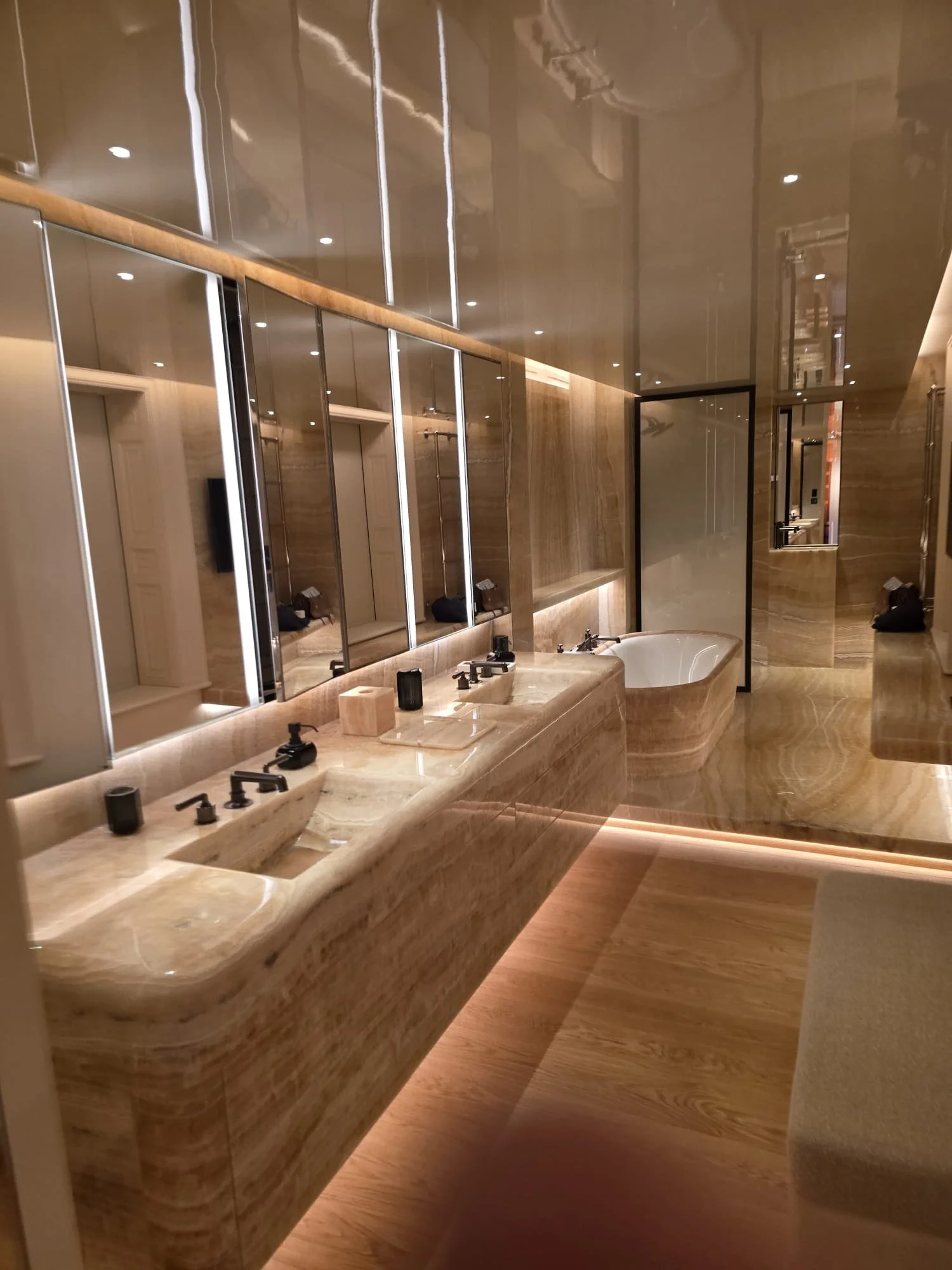 Luxurious marble bathroom with double sinks, illuminated mirrors, freestanding bathtub, and warm wood flooring