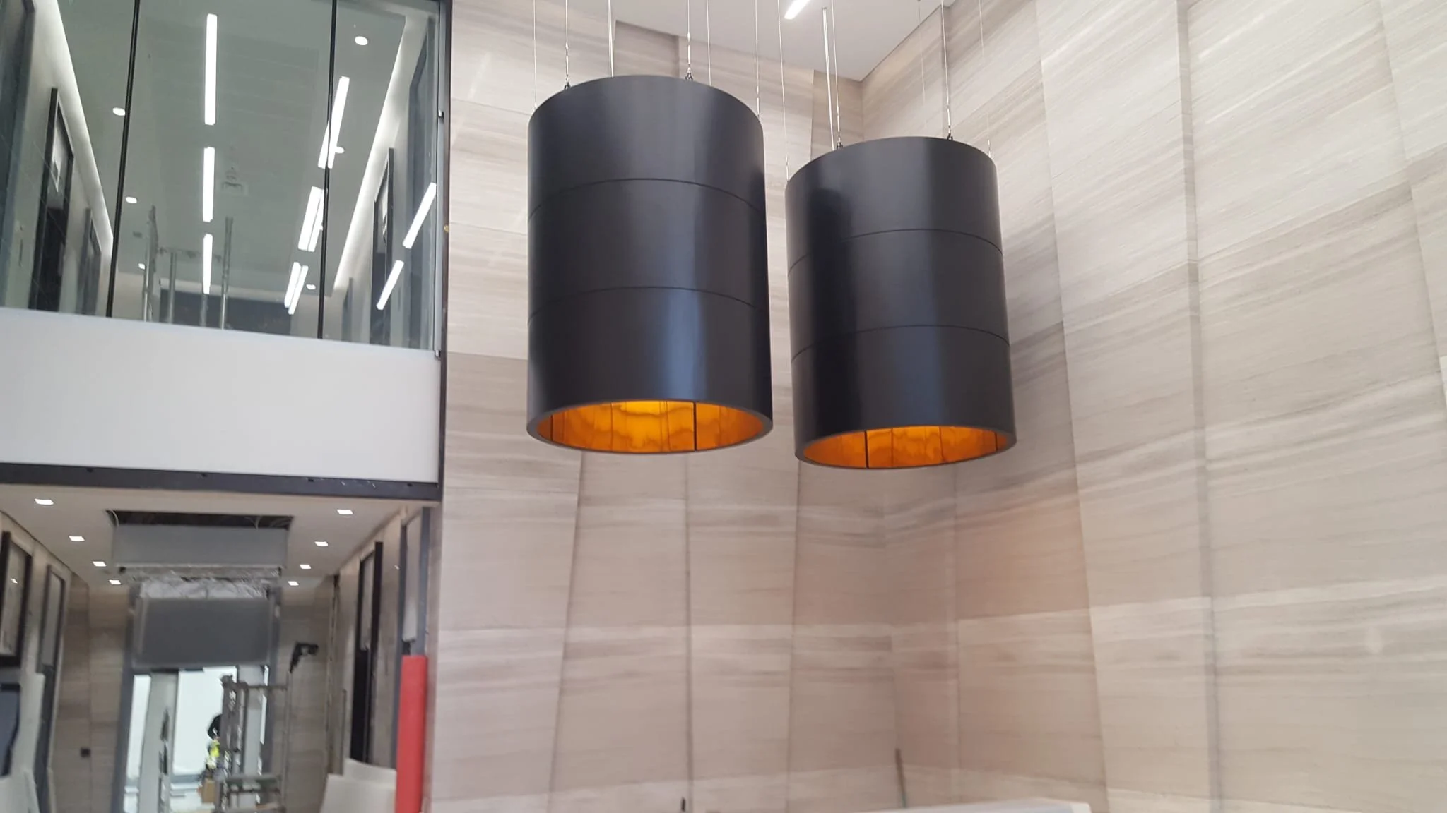 Two large black cylindrical pendant lights with warm orange interiors hanging in a modern marble lobby.