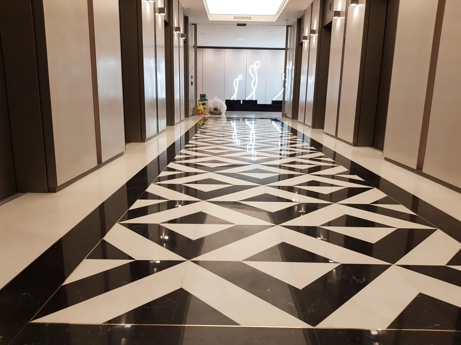 Luxurious hotel hallway with a glossy black-and-white geometric marble floor, paneled walls, and illuminated abstract artwork at the far end