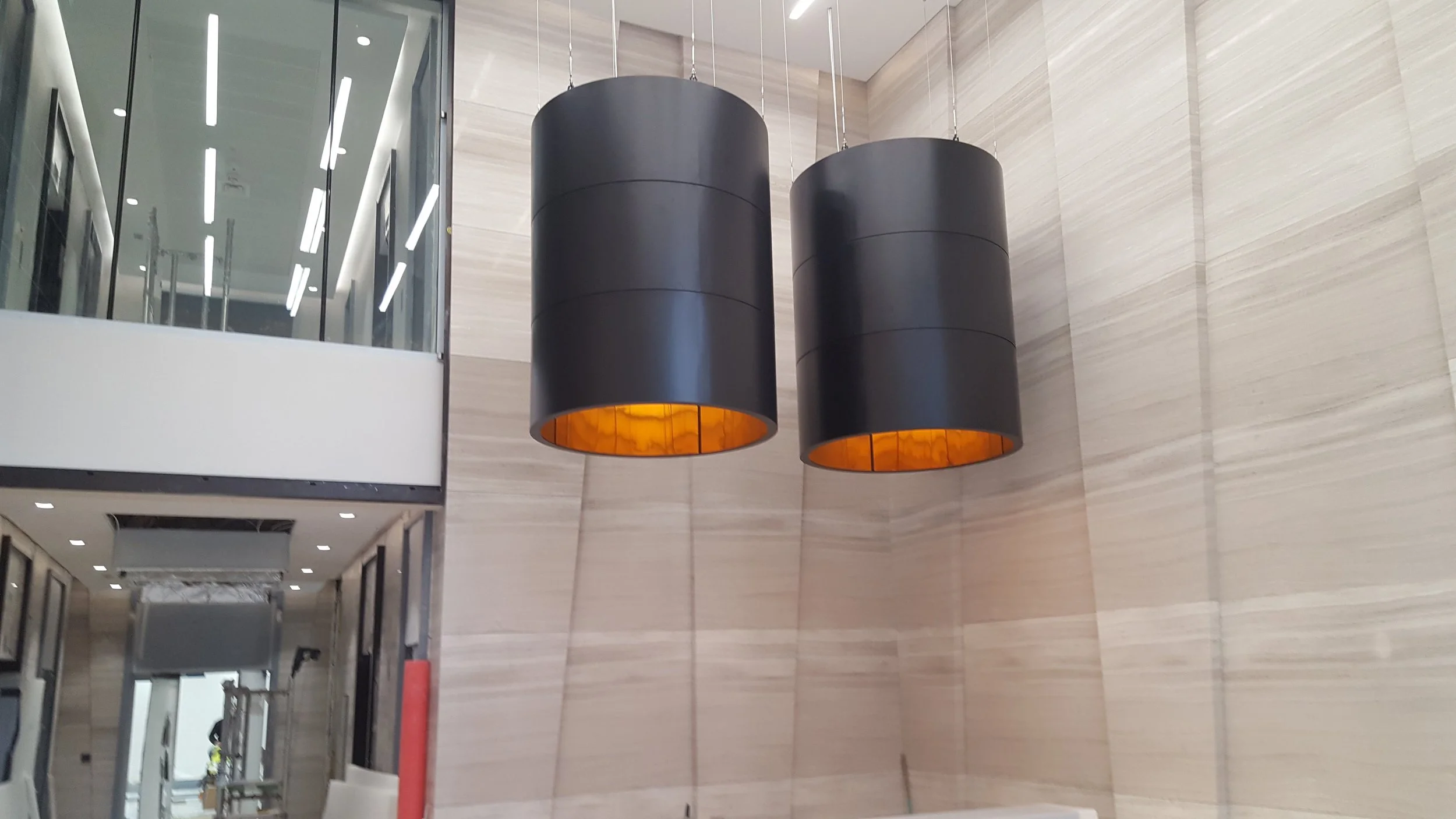 Two large black cylindrical pendant lights with glowing orange interiors in a modern lobby.