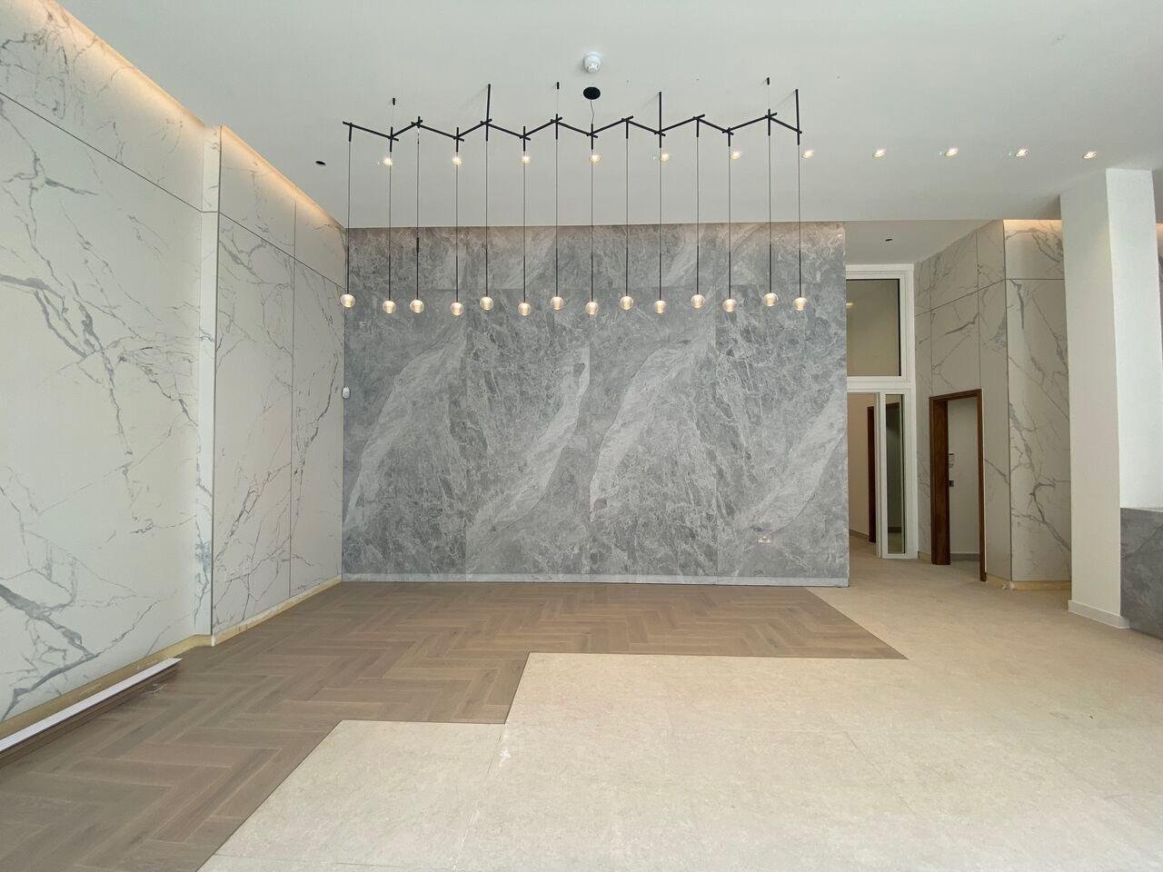 Modern marble-clad interior with gray stone accent wall, white marble walls, herringbone wood flooring, and linear pendant lights
