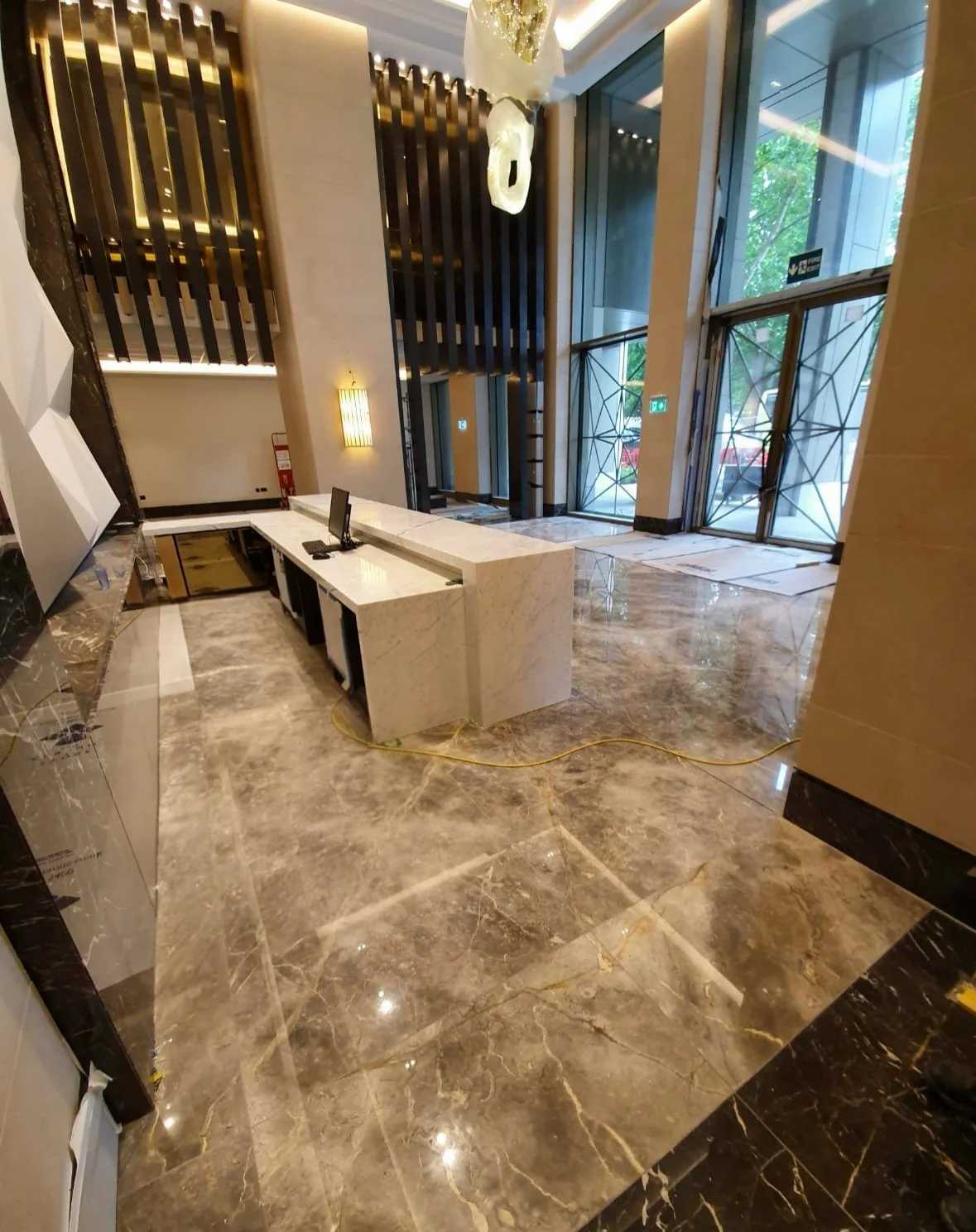 Elegant modern hotel lobby with marble reception desk, polished marble floors, decorative wall panels, pendant lighting, and tall windows.