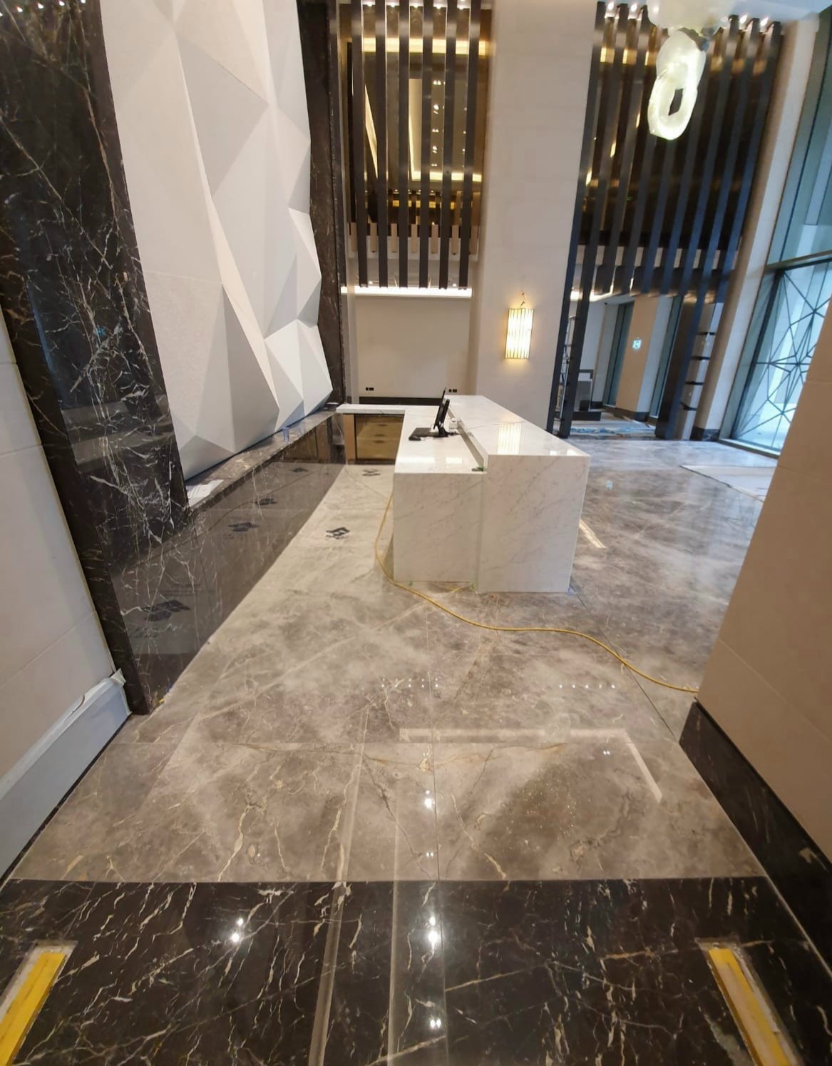 Modern hotel lobby reception desk with marble floors, black marble walls, geometric white sculpture, and decorative vertical slats