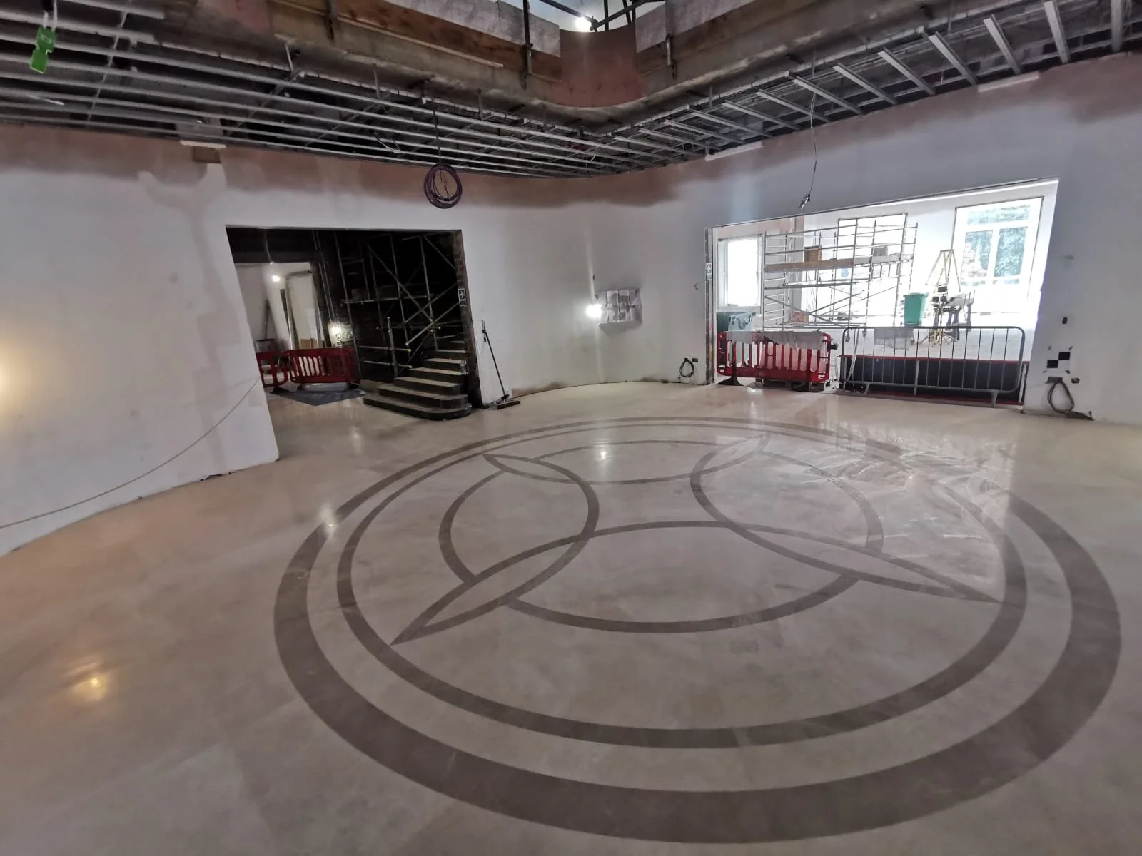 Nearly finished interior renovation with polished geometric tile flooring, exposed ceiling framework, scaffolding, and safety barriers