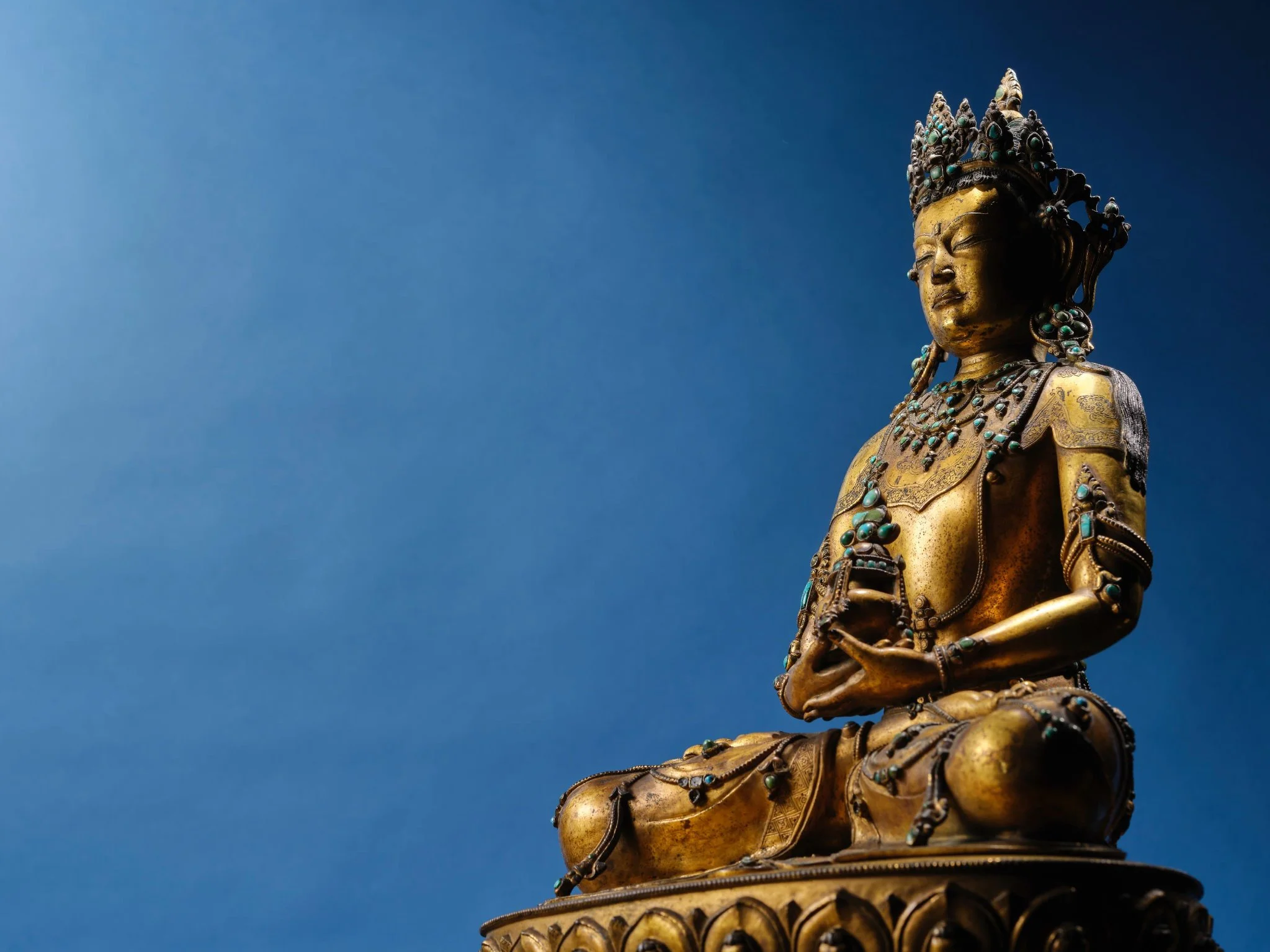 Golden Buddhist statue with turquoise accents, seated in a meditative pose against a clear blue sky.
