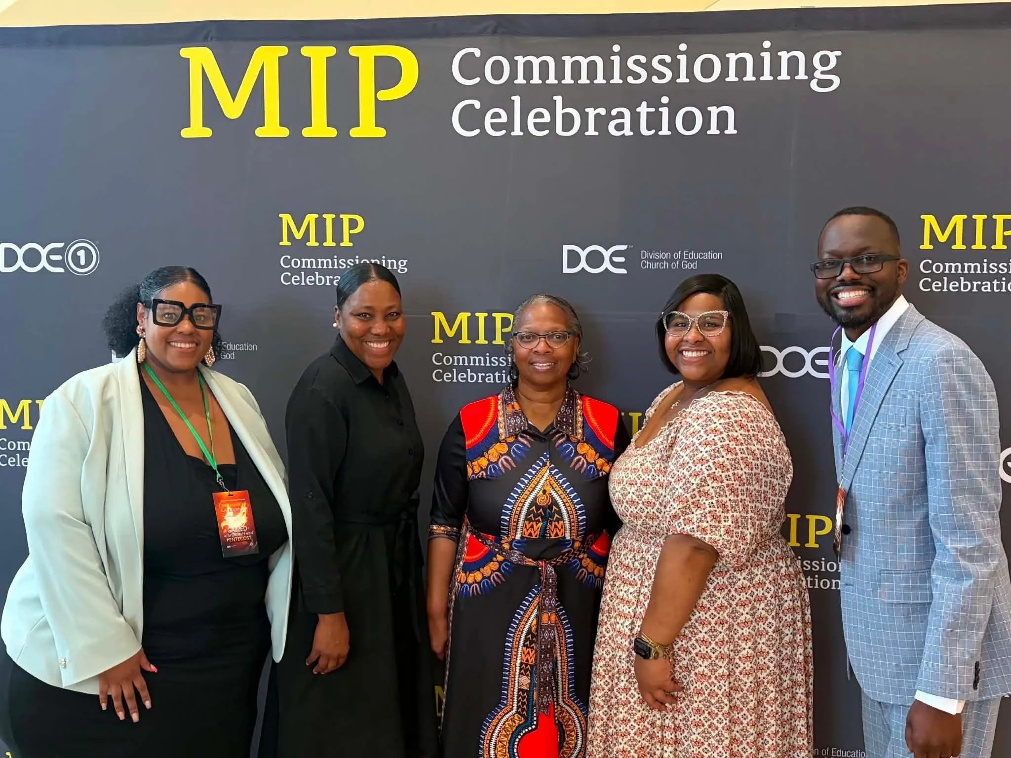 Lion of Judah Community Church people standing in front of a black backdrop with yellow and white text that reads 'MIP Commissioning Celebration'.