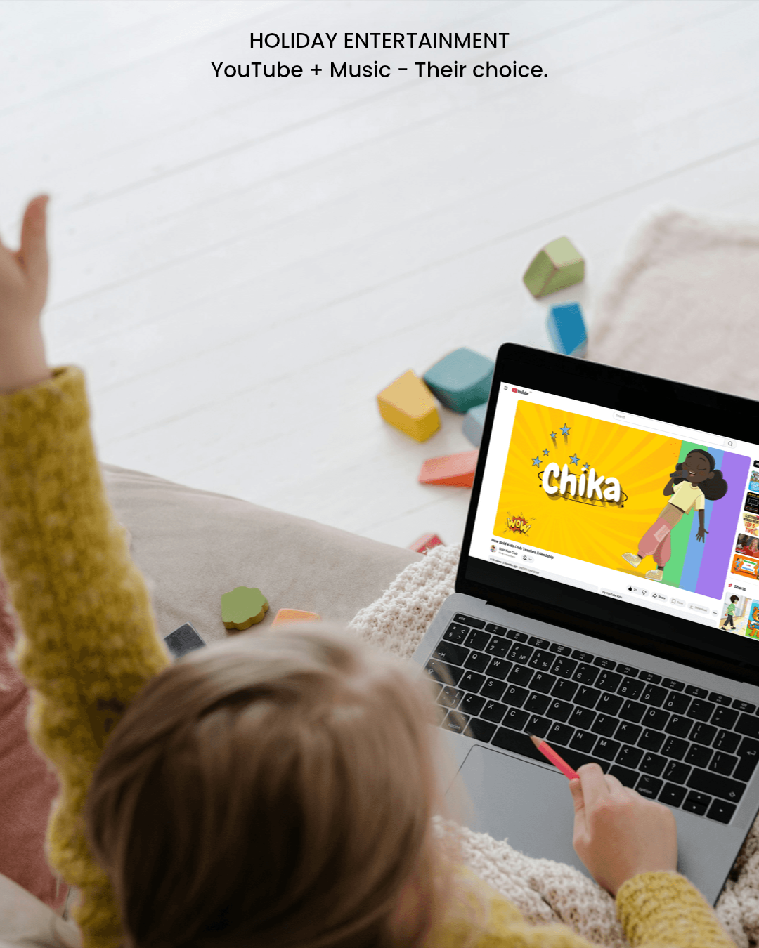 Child watching a YouTube video from Bold Kids Club titled 'Chika' on a laptop, with colorful blocks scattered on the white floor around.