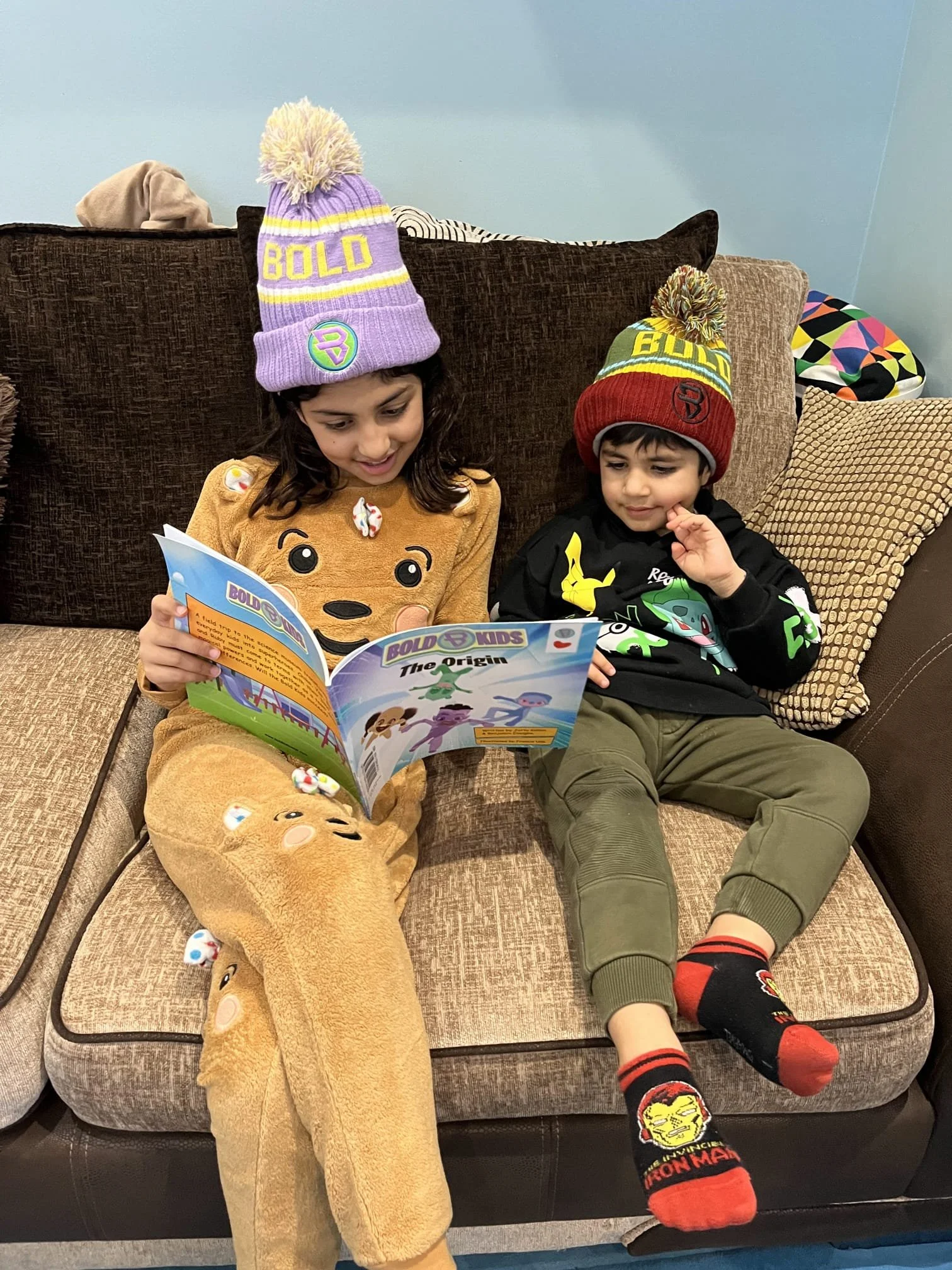 Brother and sister wearing the bold kidswear beanie and reading the bold kids book at home