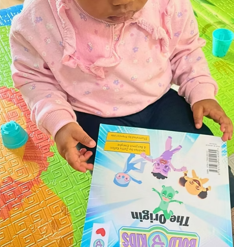 toddler girl holding the bold kids the origin book smiling