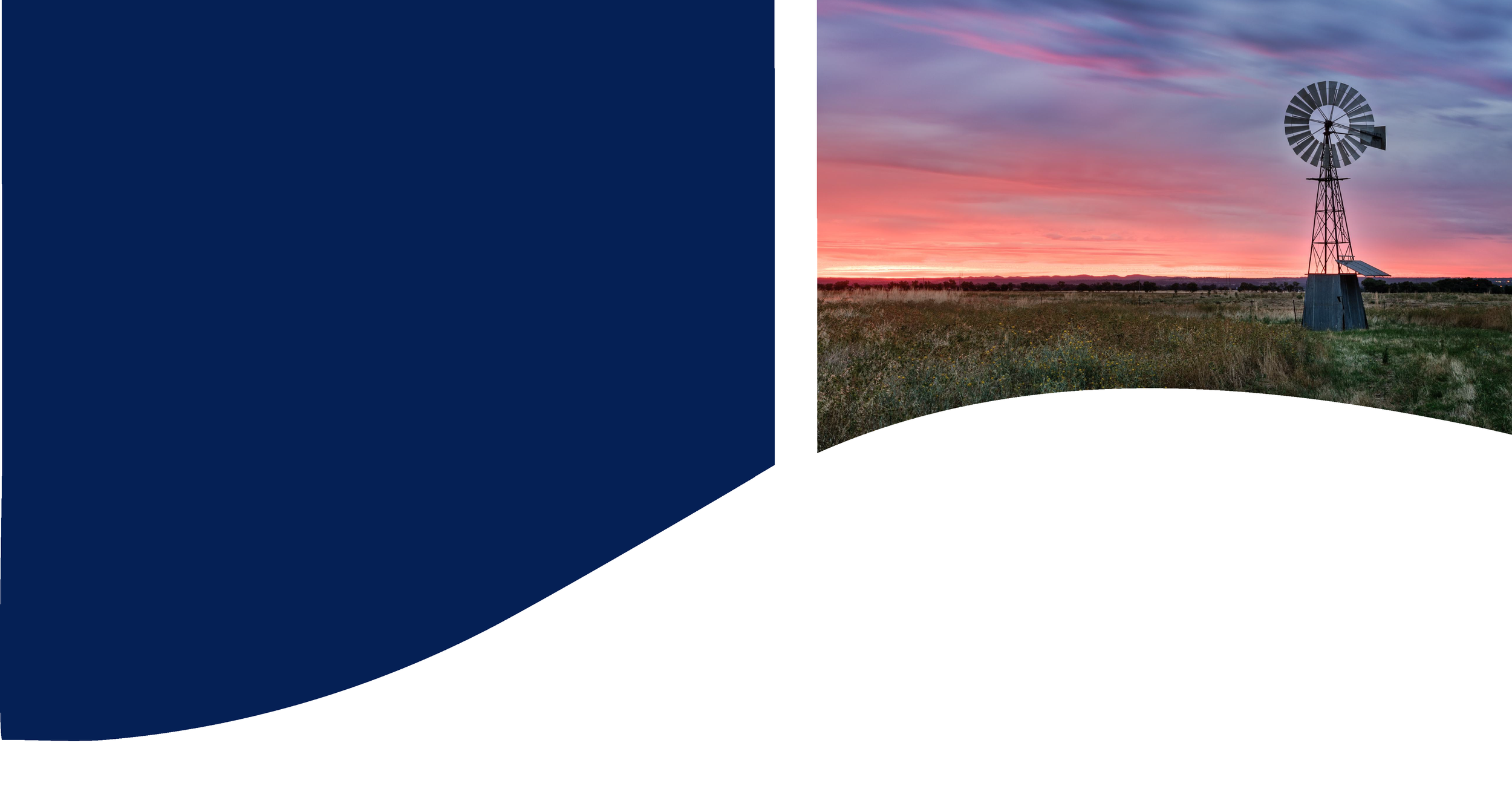 A windmill standing in a grassy field during sunset or sunrise with a colorful sky with orange, pink, and purple hues.