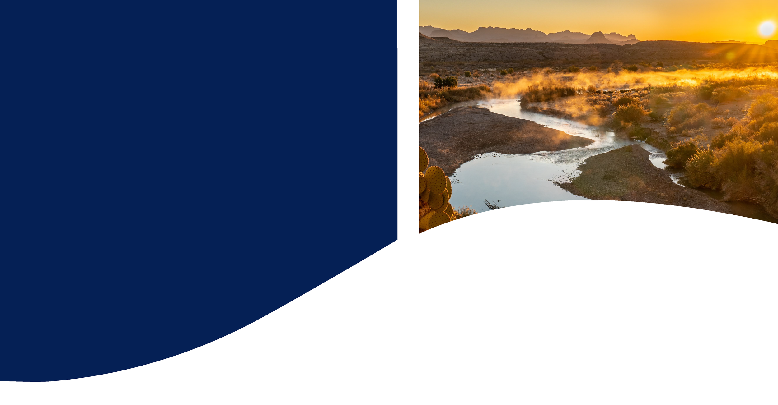A scenic view of a river flowing through a desert landscape at sunset with mountains in the background.