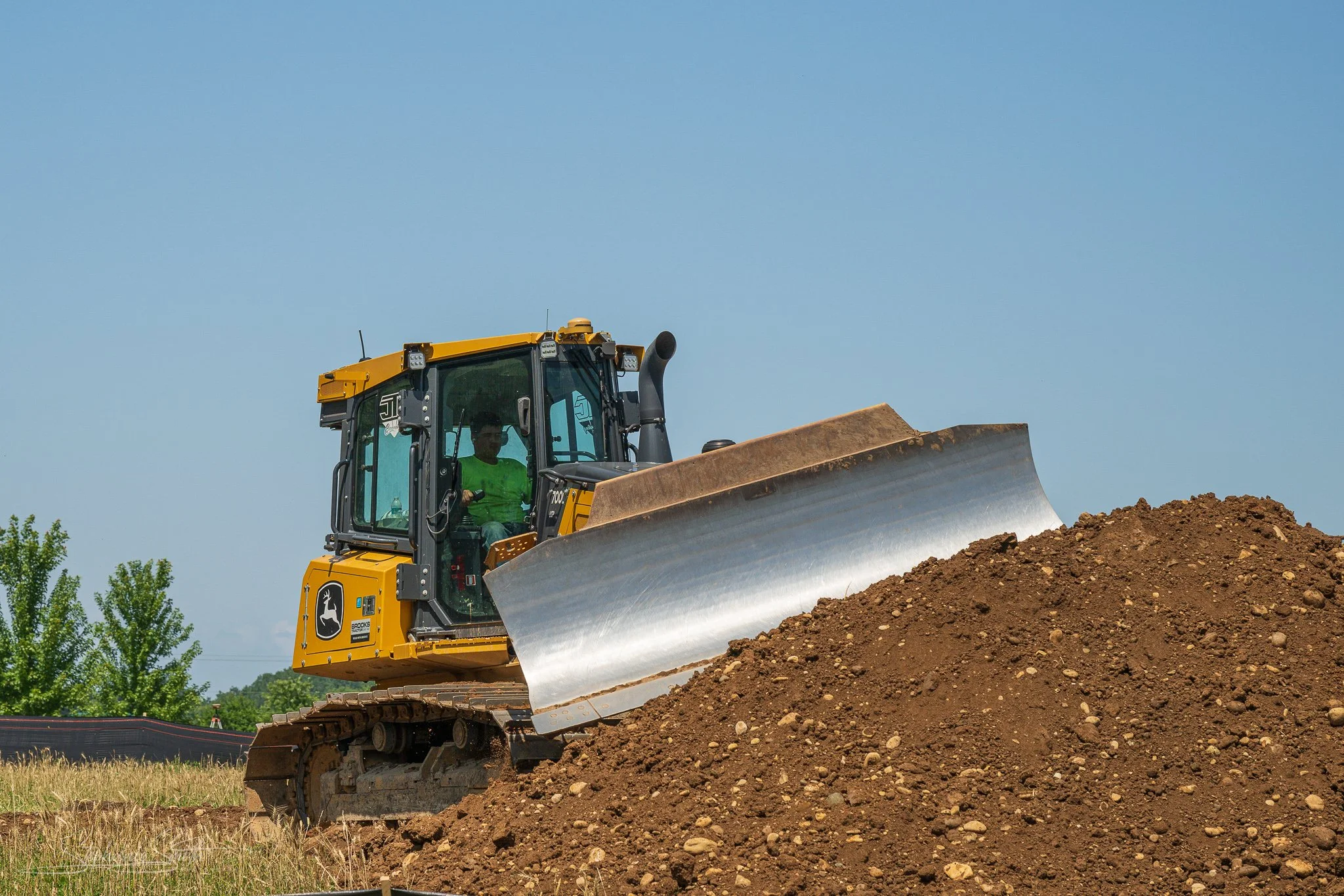 A yellow bulldozer working on a construction site with a clear blue sky in the background and some greenery on the side.