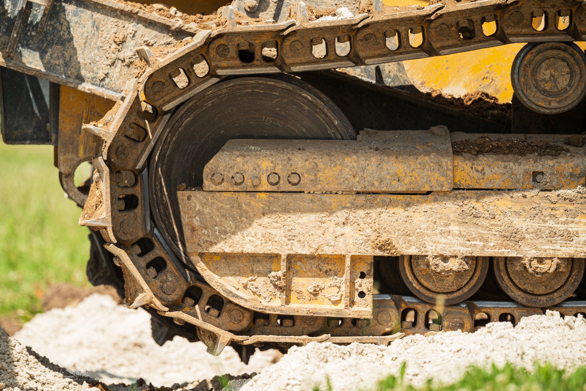 Close-up of a bulldozer's rubber track with dirt and soil on it, operating on a construction site with some grass in the background.