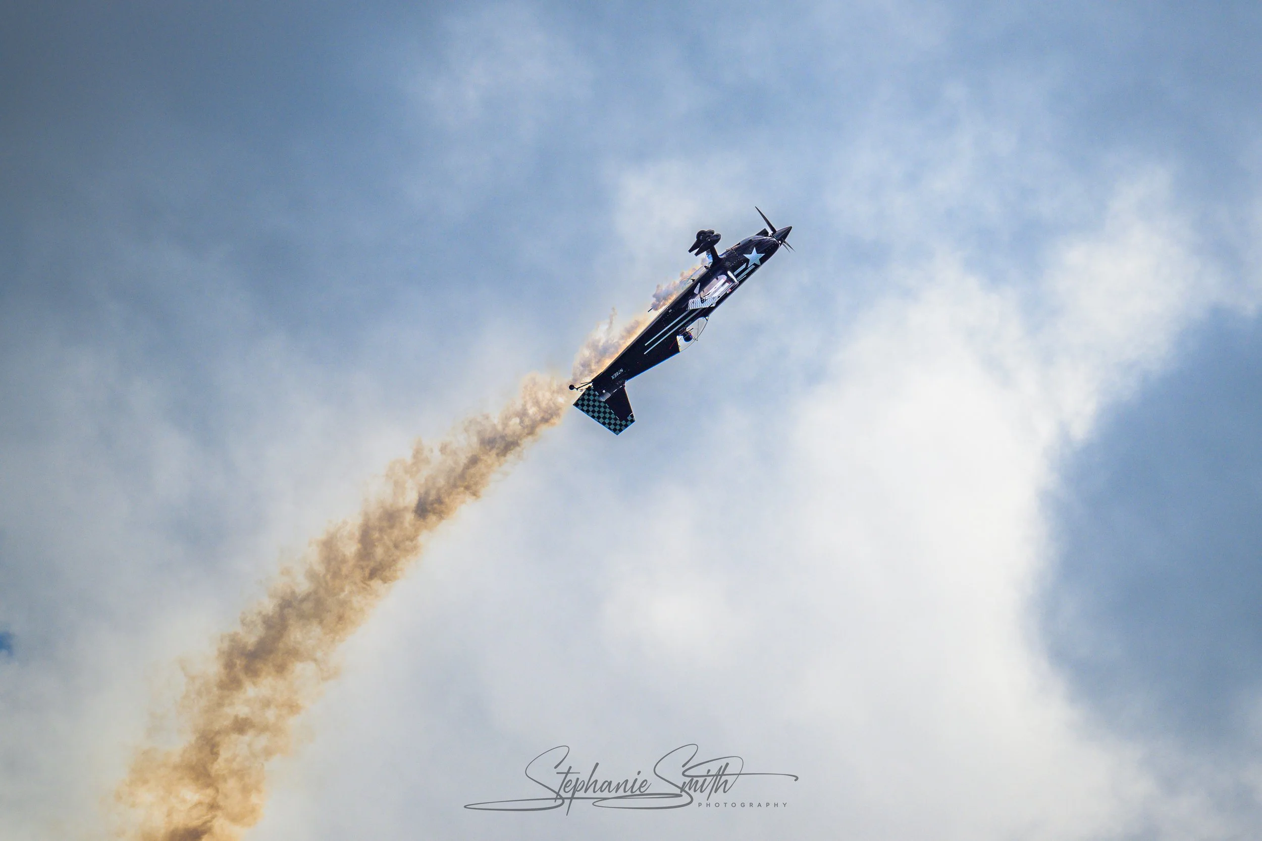 A jet airplane releasing colored smoke as it flies in the sky with clouds in the background.