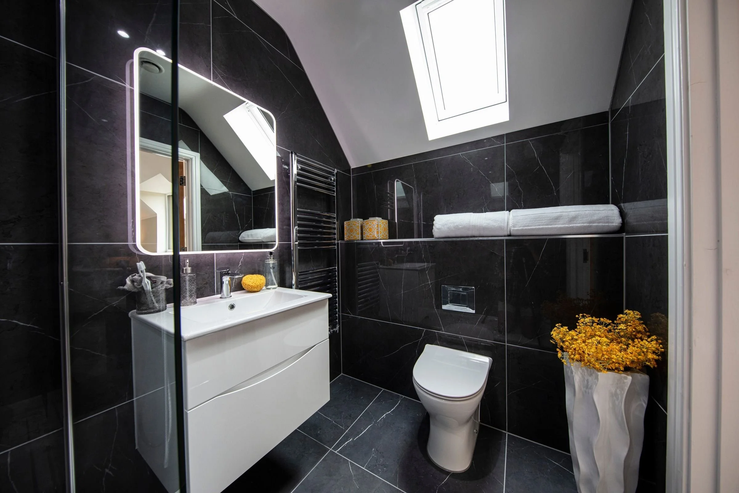 Guest ensuite with a rooflight, illuminated mirror and dark marble-effect tiling.