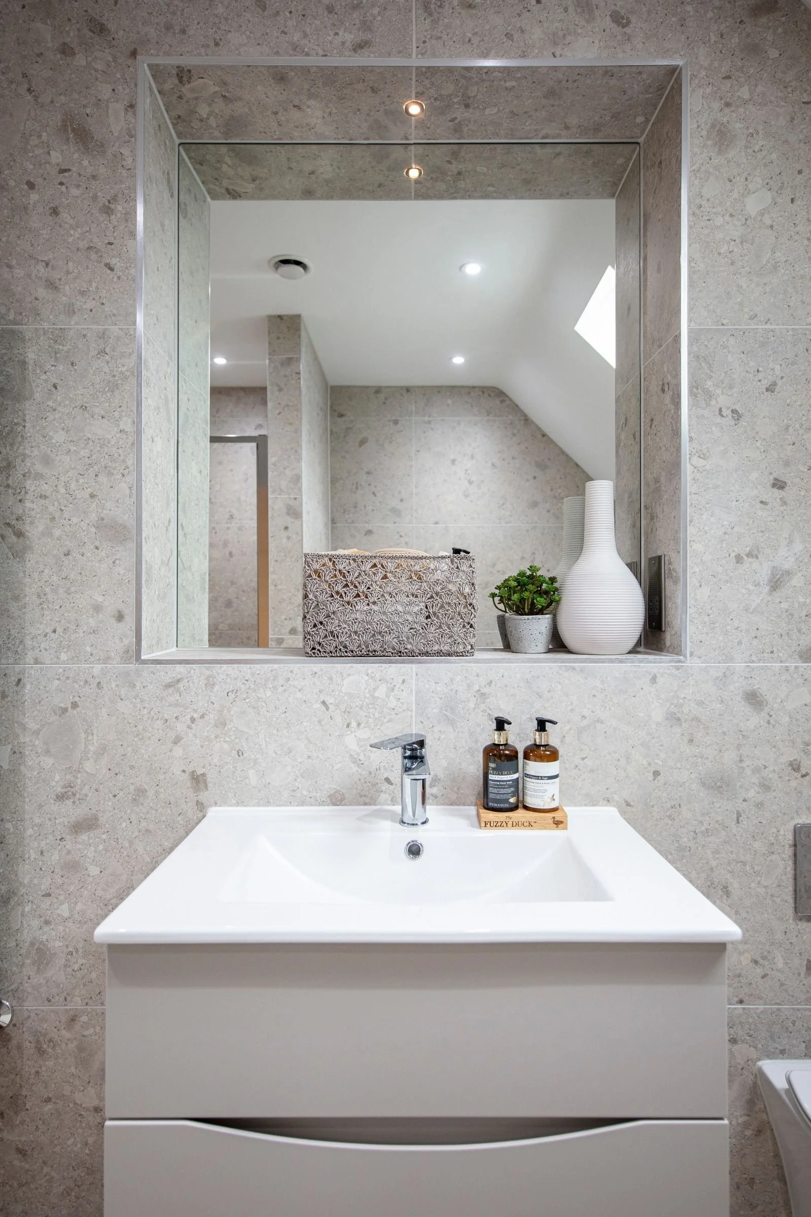 Recessed bathroom mirror framed by marble-effect tiling.