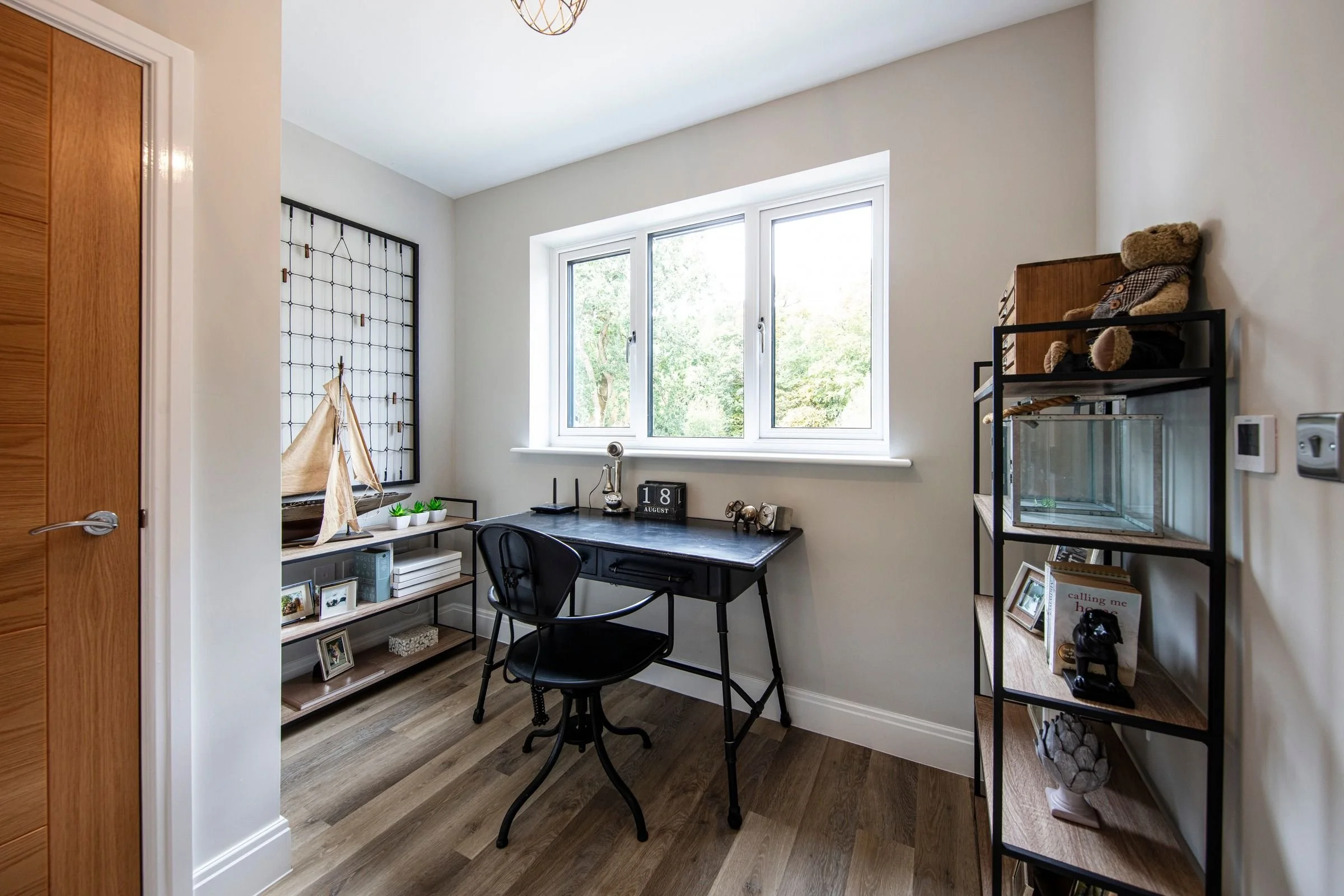 Naturally lit study with a wide window and wood-effect flooring.