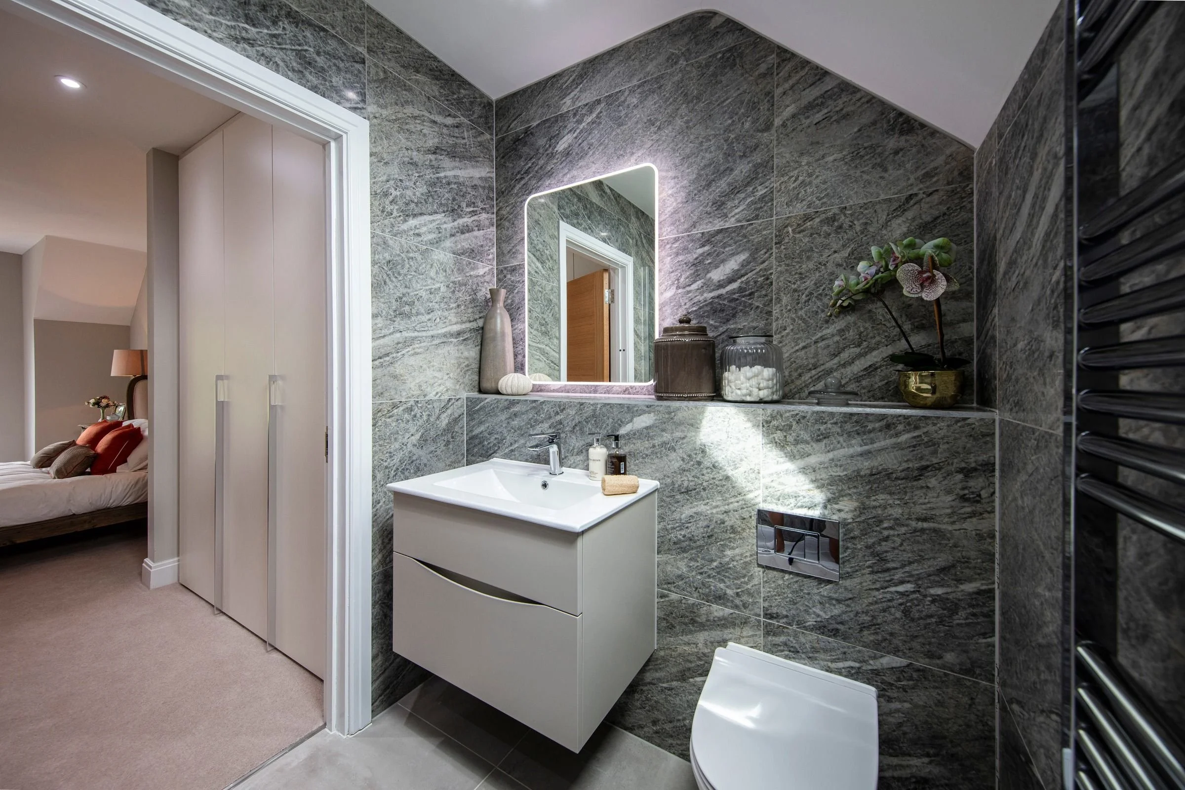 Primary ensuite with an illuminated mirror, wall-hung vanity and grey marble-effect tiling.