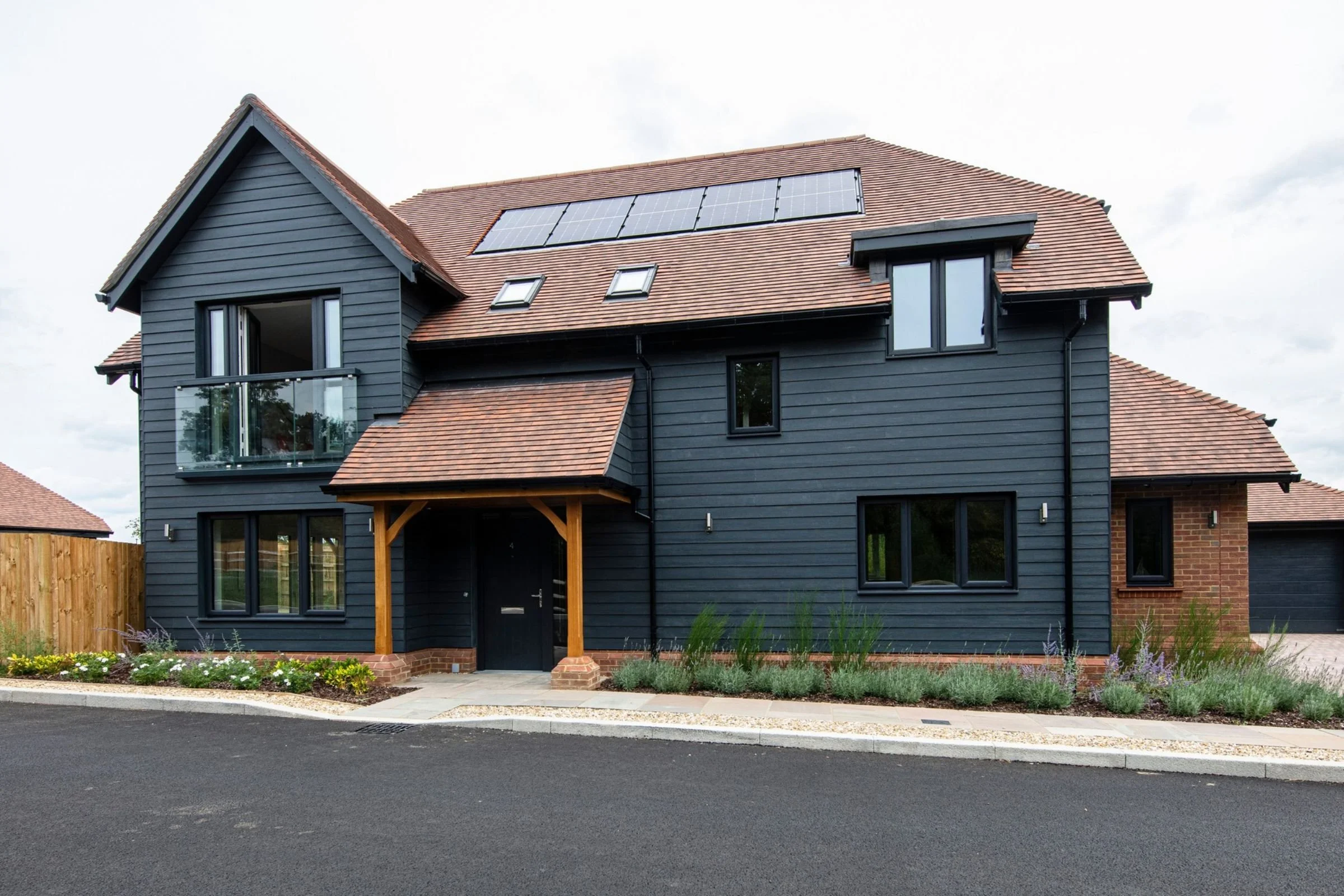 Front elevation with dark weatherboard cladding, a timber porch and solar panels.