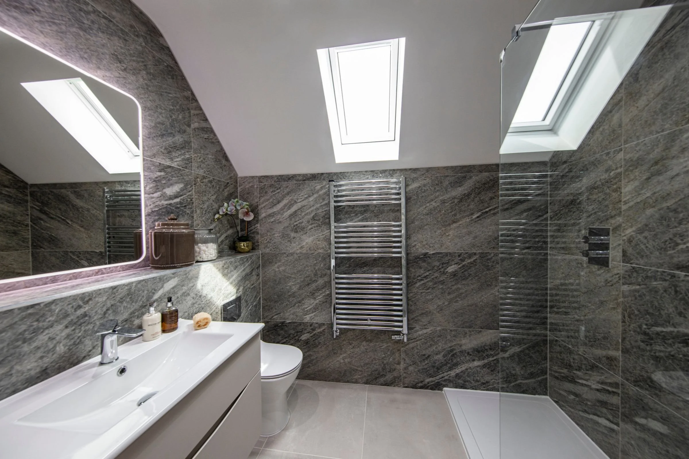 Primary ensuite with rooflights, glass shower enclosure and grey marble-effect tiling.