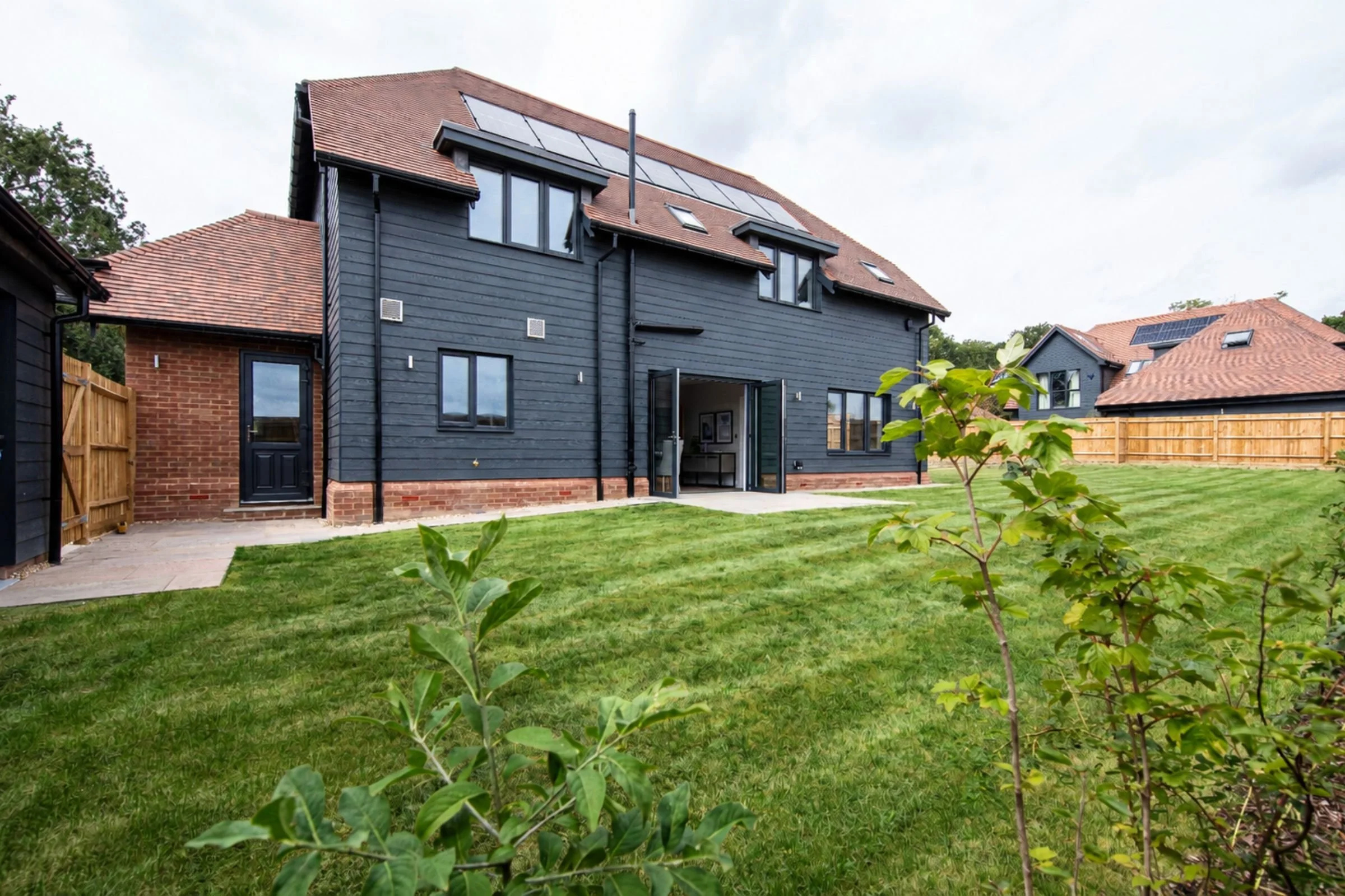 Rear elevation with open bifold doors, lawn and solar panels.