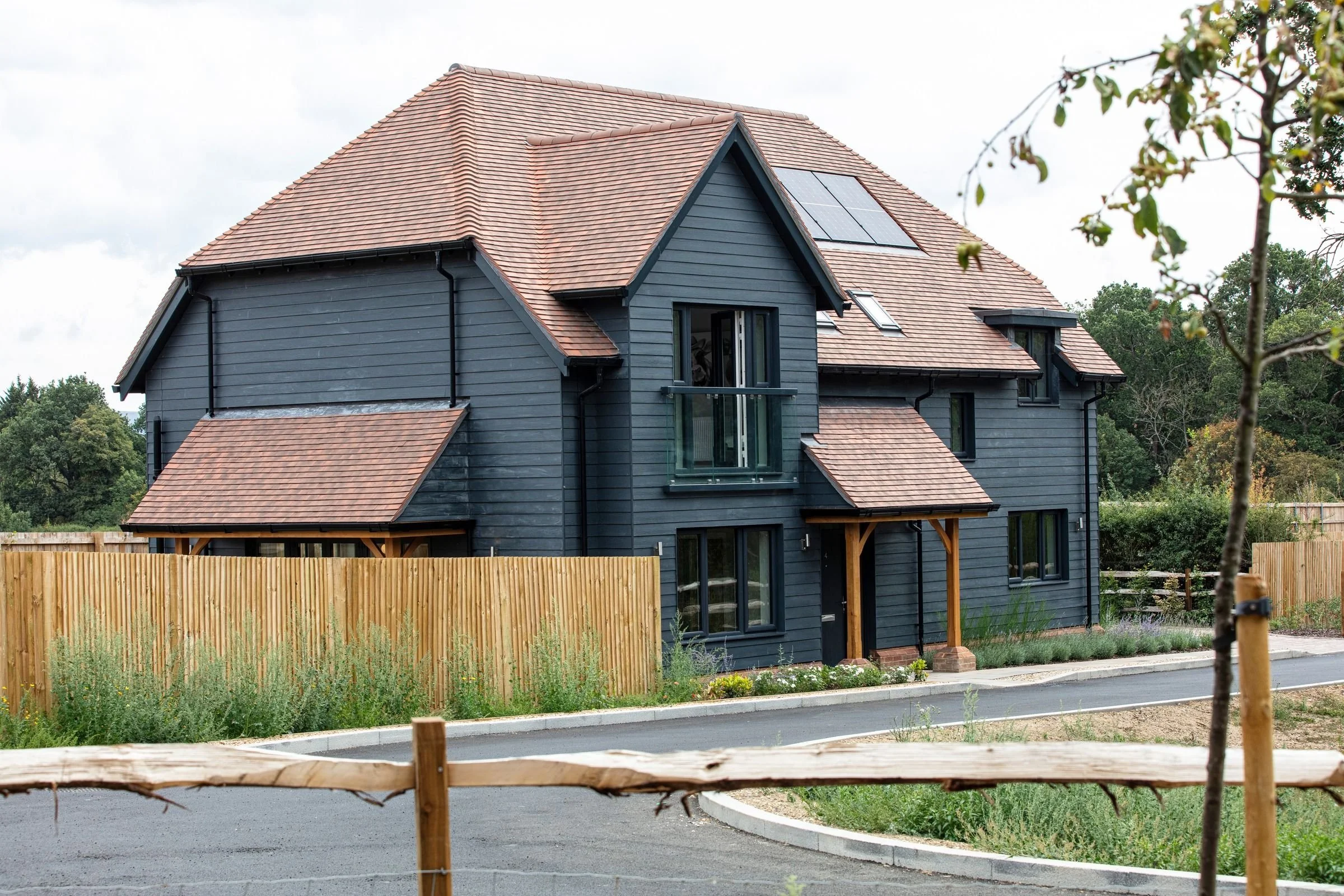 Side view of the house showing the dark weatherboard cladding and tiled roof.