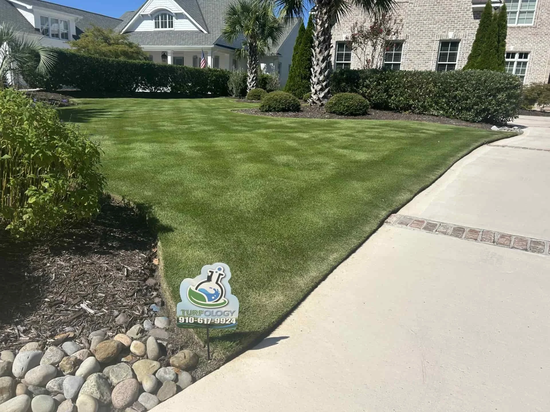 Healthy, edged lawn along a curved driveway with a Turfology yard sign at a residential property in Wilmington, NC