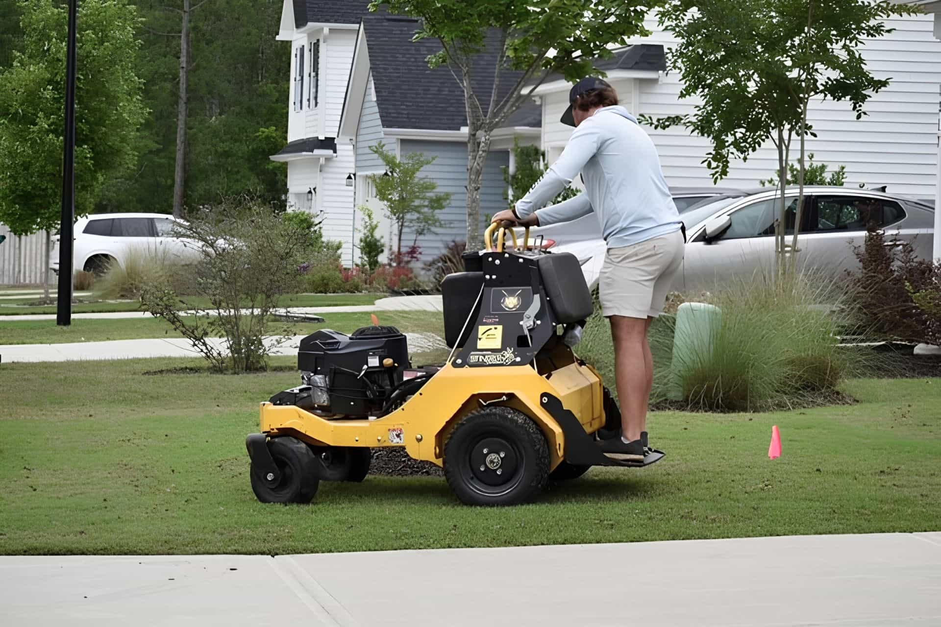 Turfology technician operating a stand-on aerator on a residential lawn near a driveway in Wilmington, NC