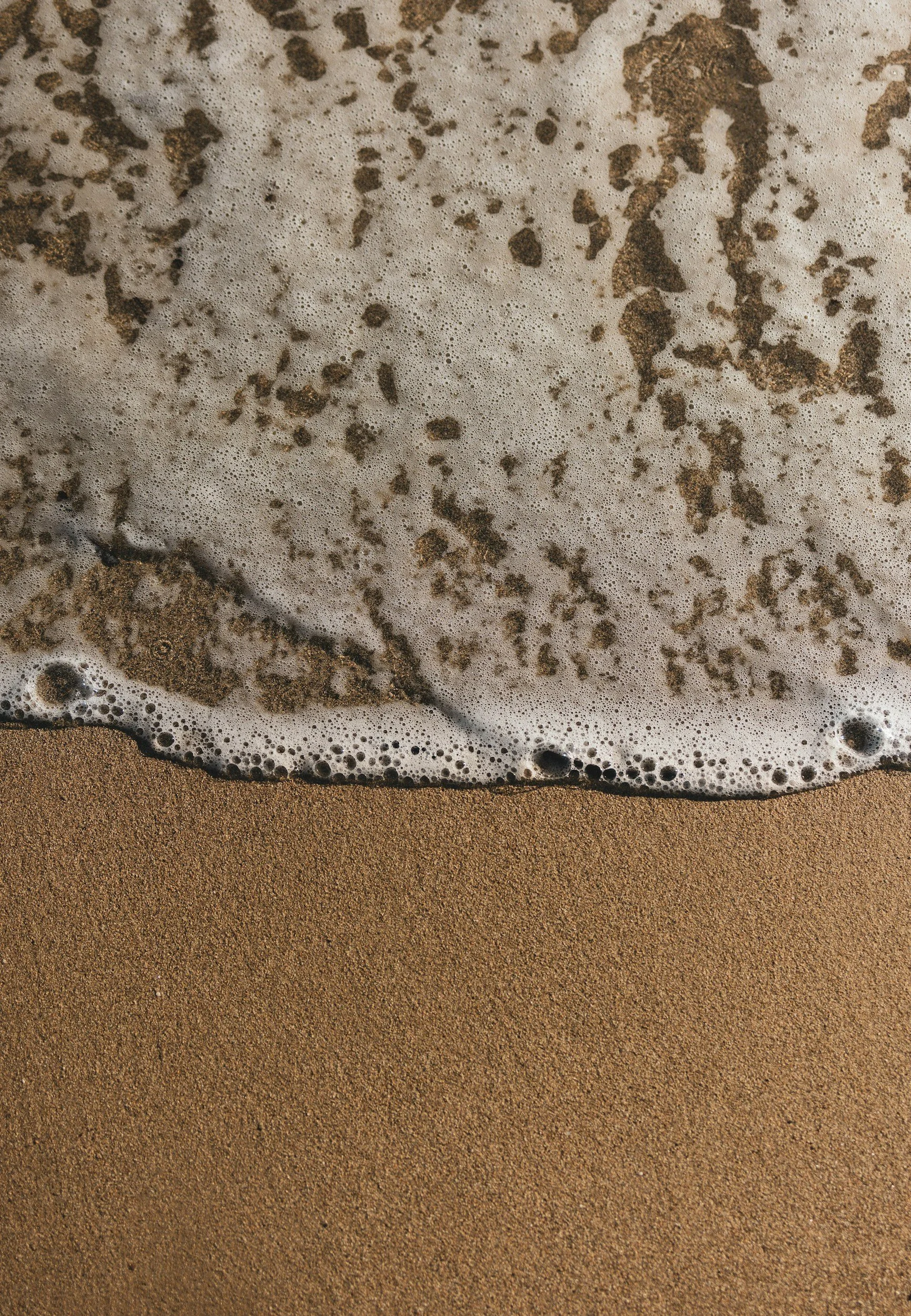 Foaming seawater washing onto sandy beach shore.