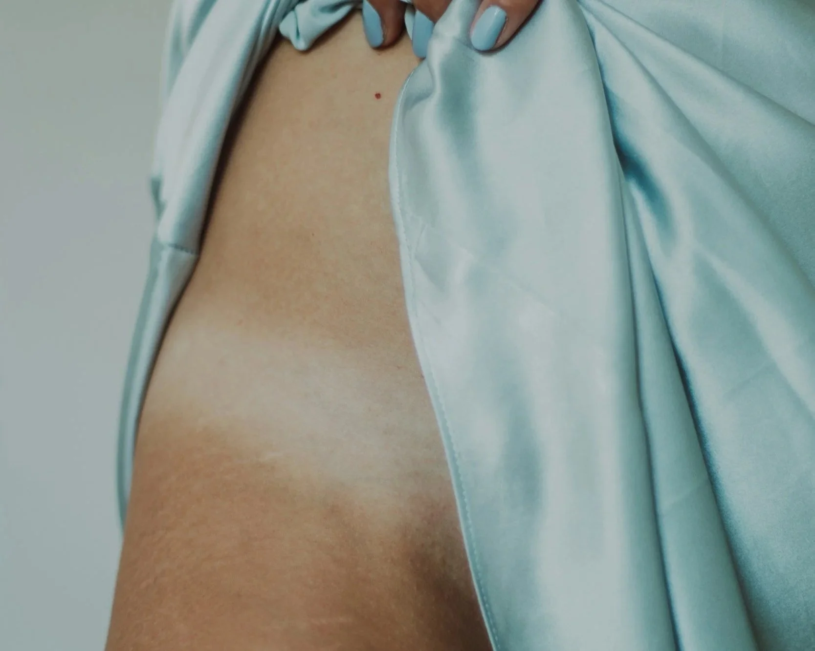 Close-up of a person's chest and shoulder area with a small red spot, partially covered by light blue satin fabric.
