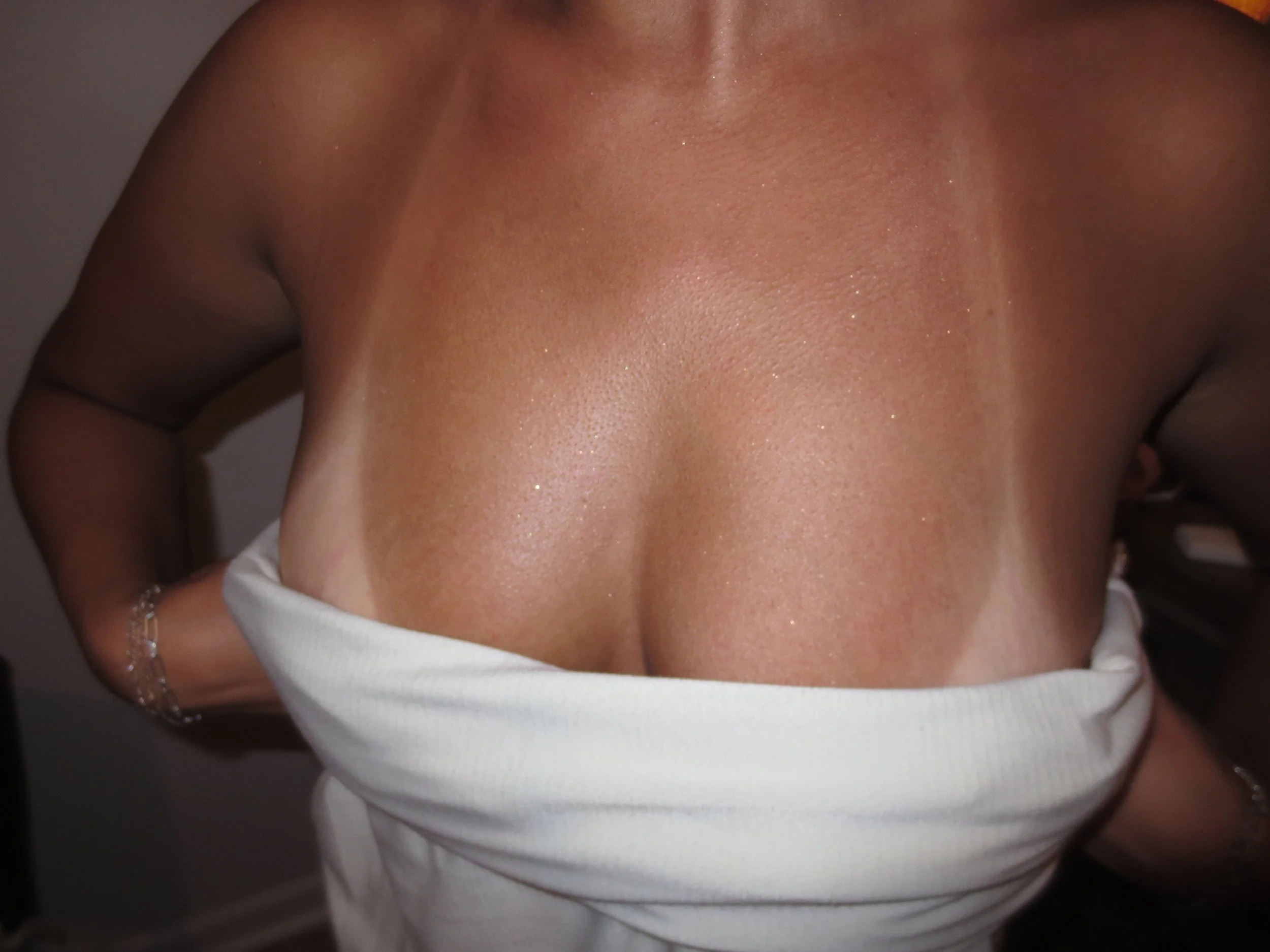 Close-up of a person's bare shoulders, collarbone, and upper chest, with a white clothing item at the bottom of the image.