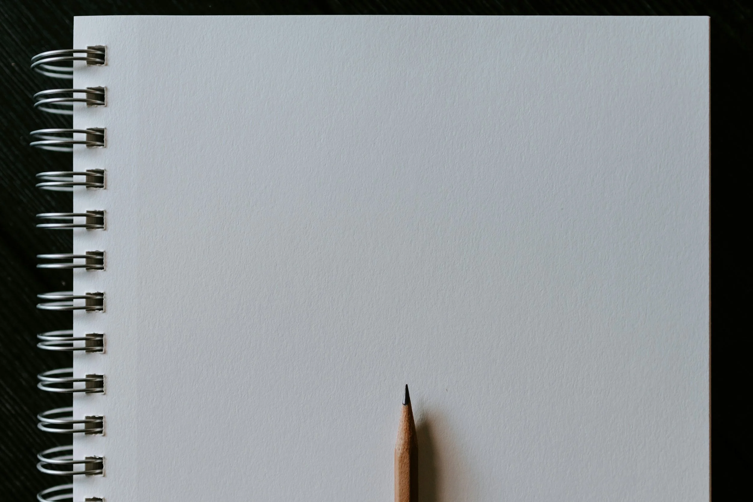 Close-up of a blank spiral-bound notebook with a sharpened pencil resting on the page.