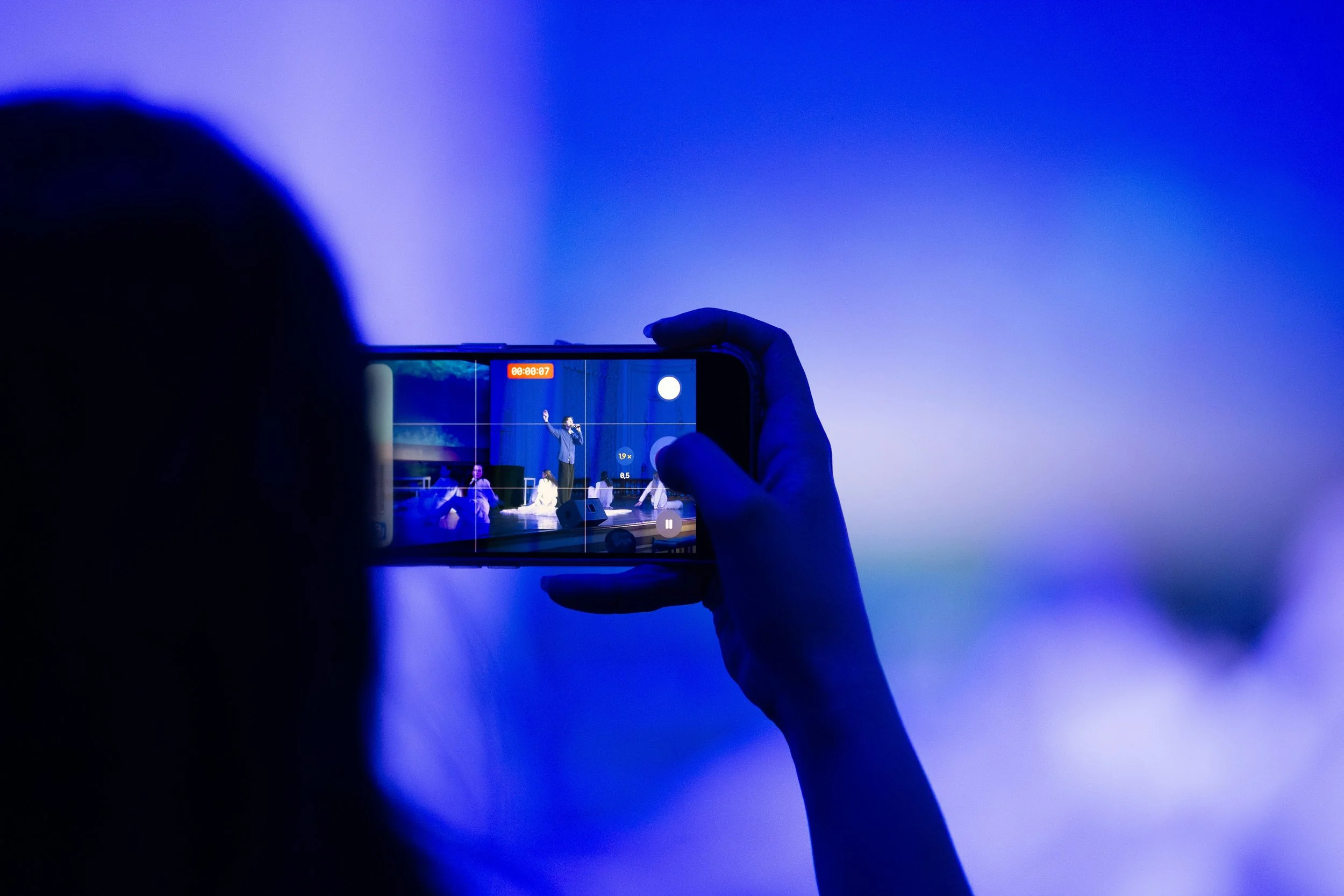 Person holding a smartphone capturing a stage performance on a dark blue background.