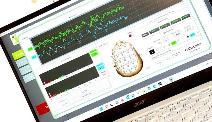Laptop screen displaying scientific LENS data graphs, a small ancient clay vessel with inscriptions, and interface controls, likely for data analysis.