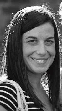 Black and white photo of a woman with long dark hair smiling, wearing a striped shirt.