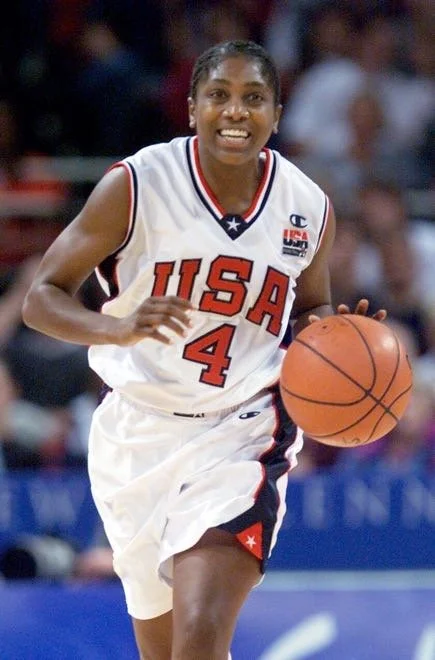 Female basketball player in a white USA jersey with number 4 dribbling a basketball during a game.