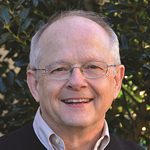 A smiling man outdoors with trees in the background.