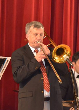 Man playing a trombone during a performance in front of red curtains.