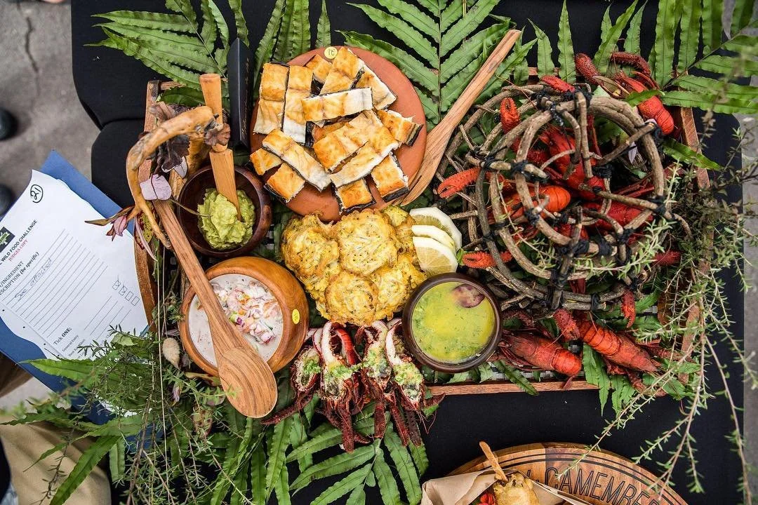 A seafood platter with fried fish, lobster, crabs, and shellfish, garnished with lemon wedges, green sauce, and scallions, served on a bed of green leaves.