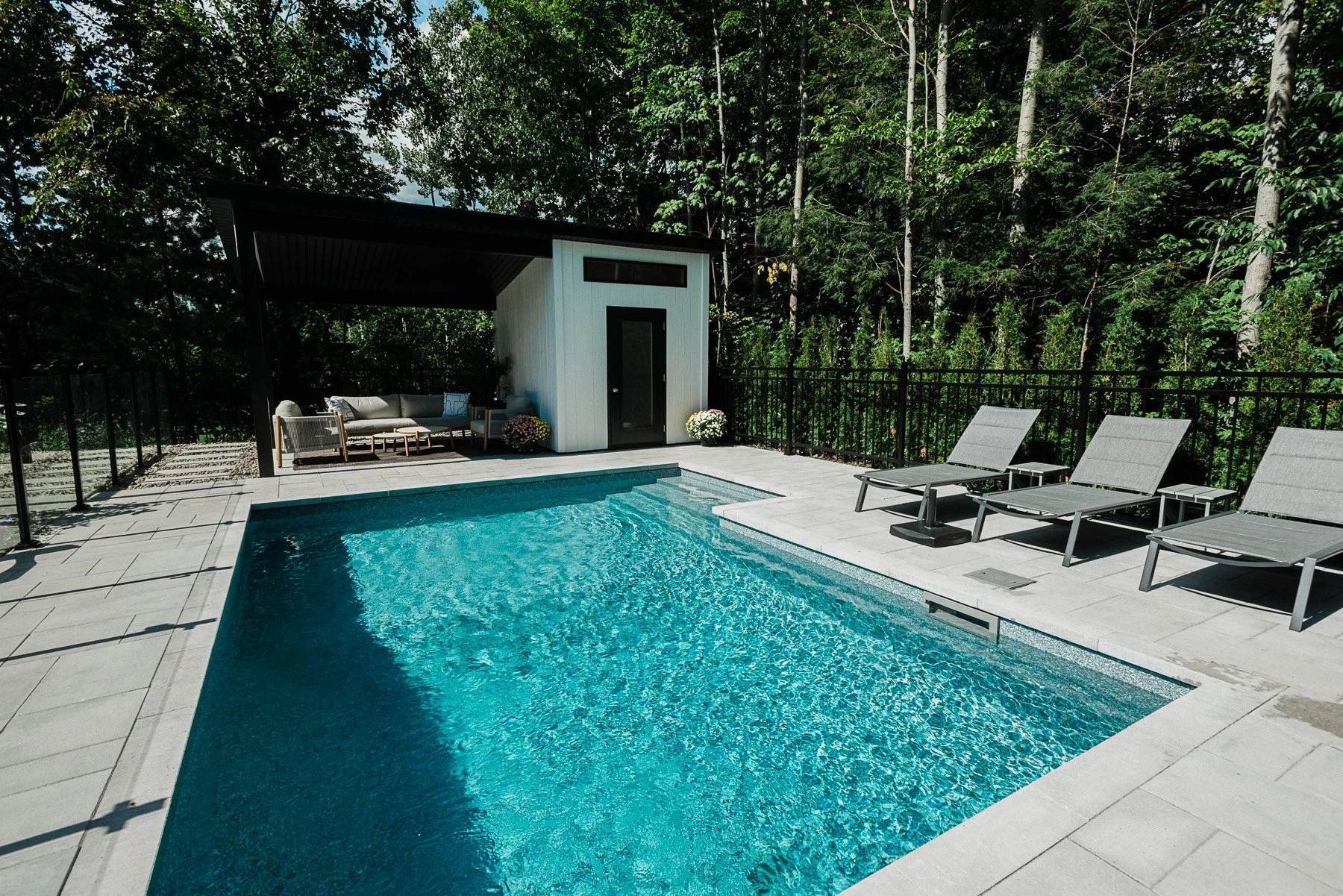 Piscine extérieure avec fauteuils et espace lounge entouré d'arbres