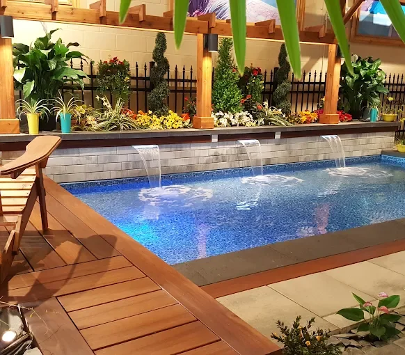 Piscine intérieure avec fontaines d'eau, entourée de plantes en pot, de fleurs et de plantes verticales, avec un sol en bois et une clôture en métal noir.