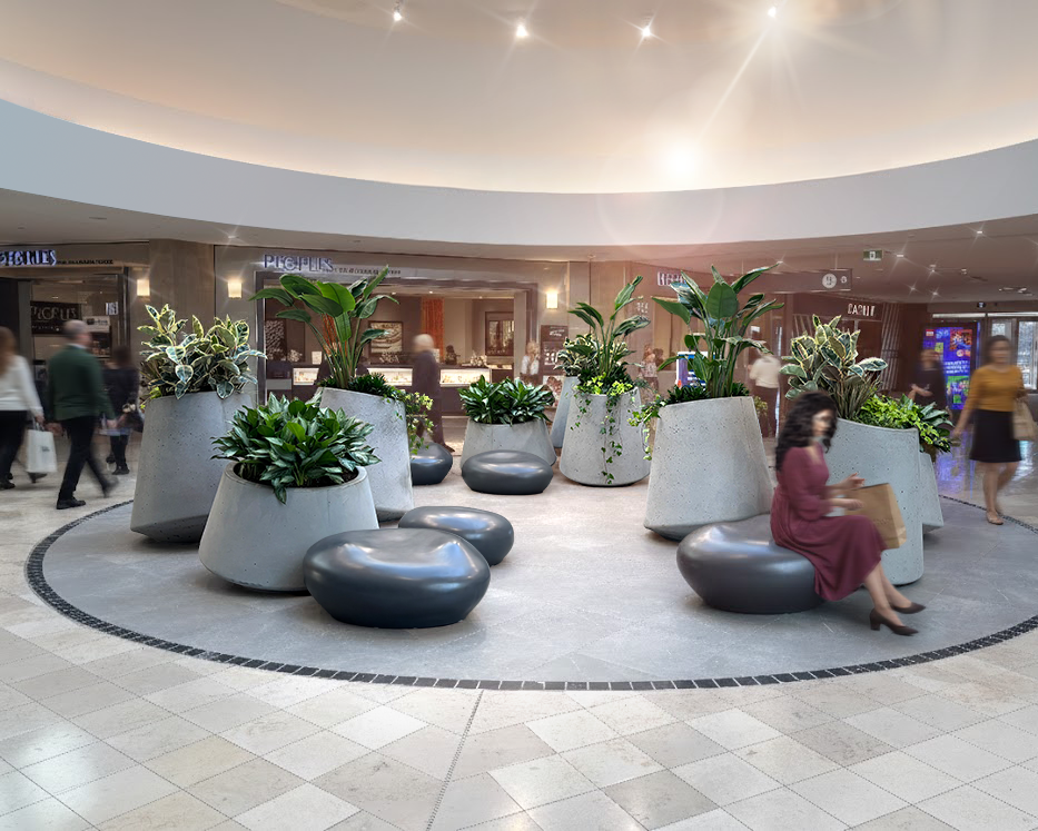 Aménagement d'un espace public intérieur intégrant de grandes jardinières verdoyantes et un assise modulaire noire évoquant la forme de galets, dans une ambiance vivante.